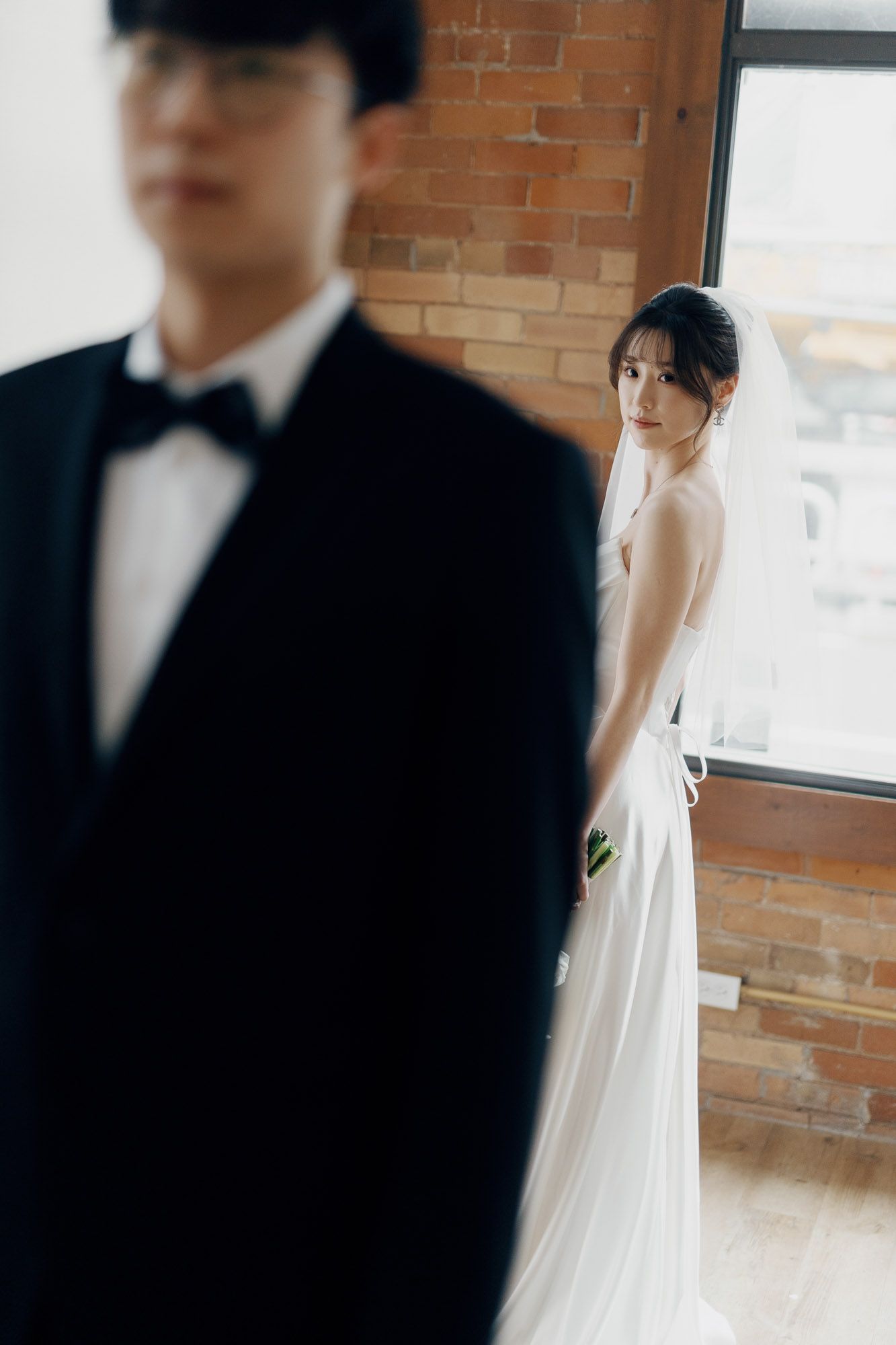 Bride looking back at groom near a brick wall window at Archive Studio in Toronto for intimate editorial wedding photography.