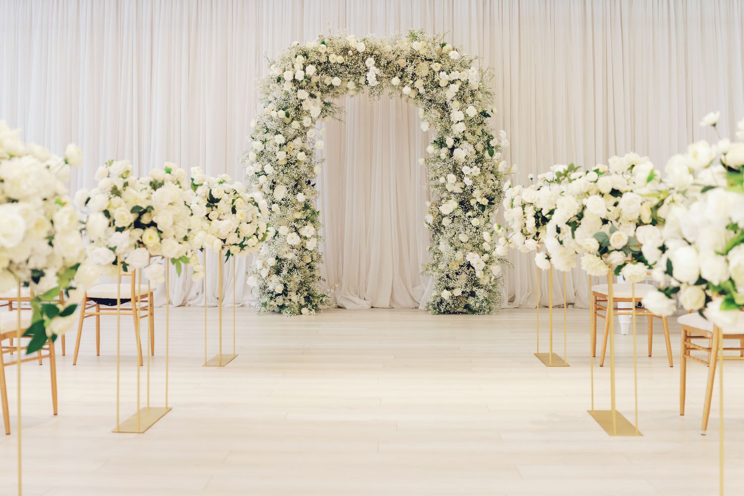 Elegant white floral ceremony arch with gold accents and draping at Bellamy Loft in North York, Toronto for wedding photography.