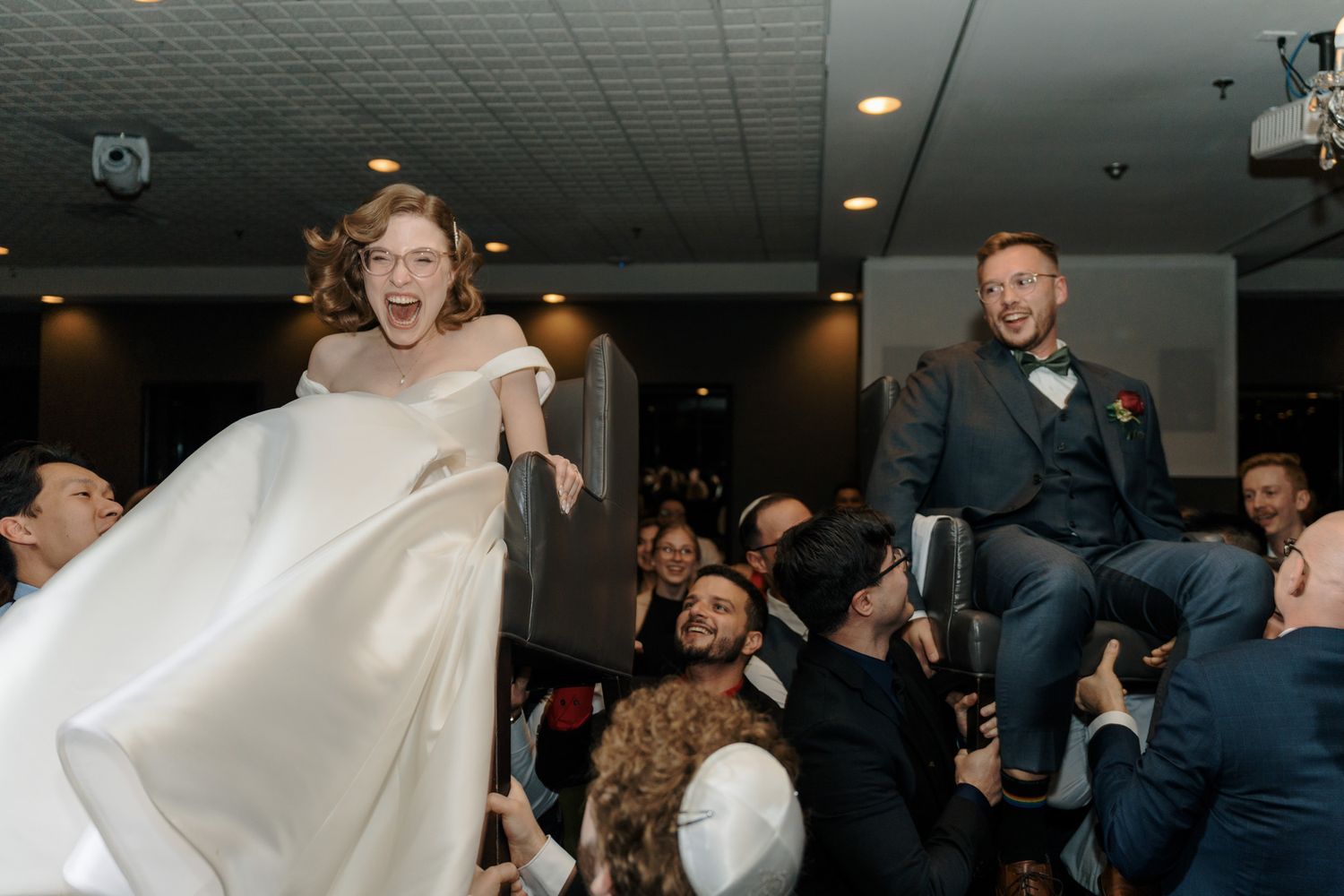 Bride and groom lifted on chairs during the hora at The Manor in King City for joyful Jewish wedding photography.
