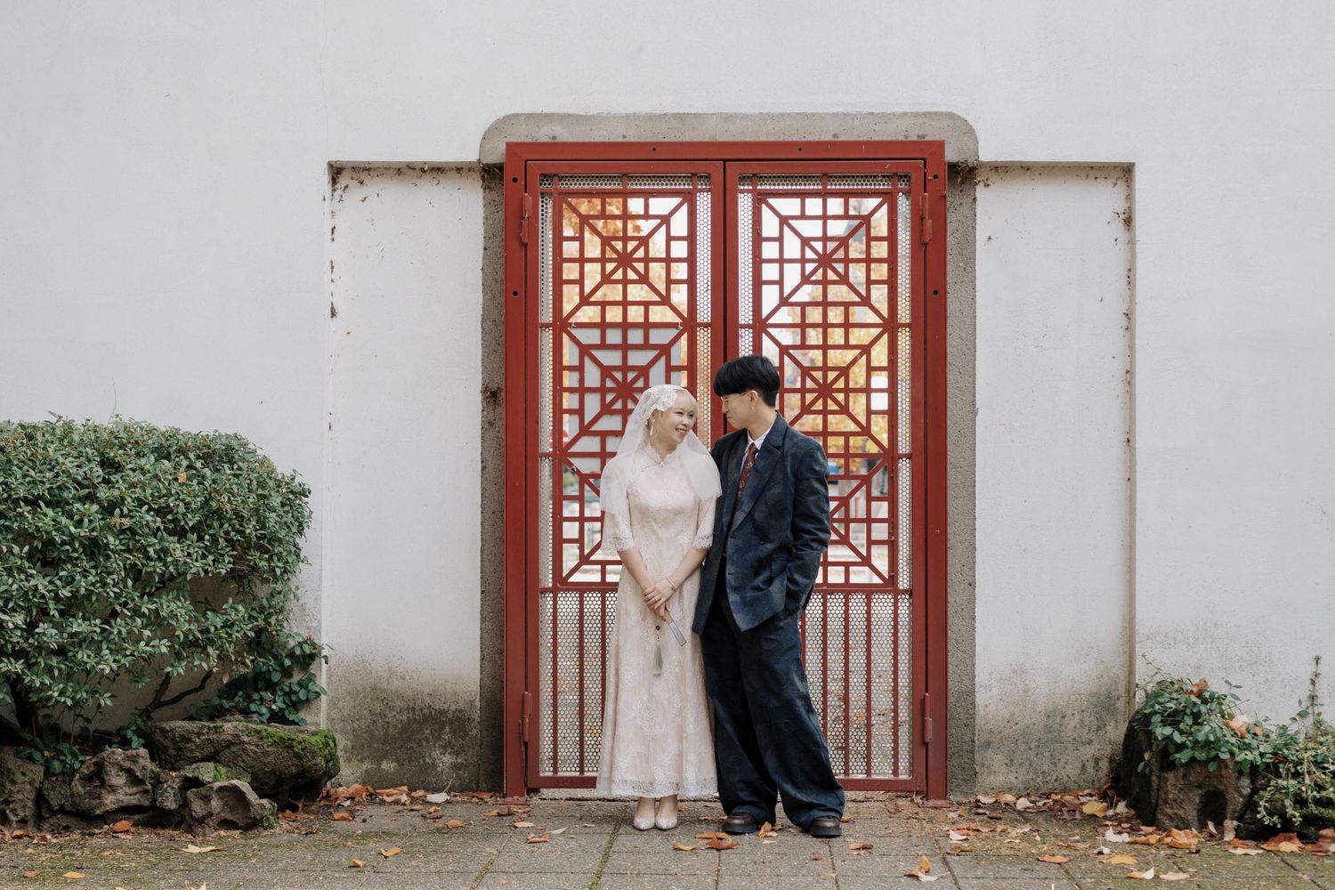 Couple in wedding attire posing before ornate red Chinese doors during a Vancouver pre-wedding portrait session