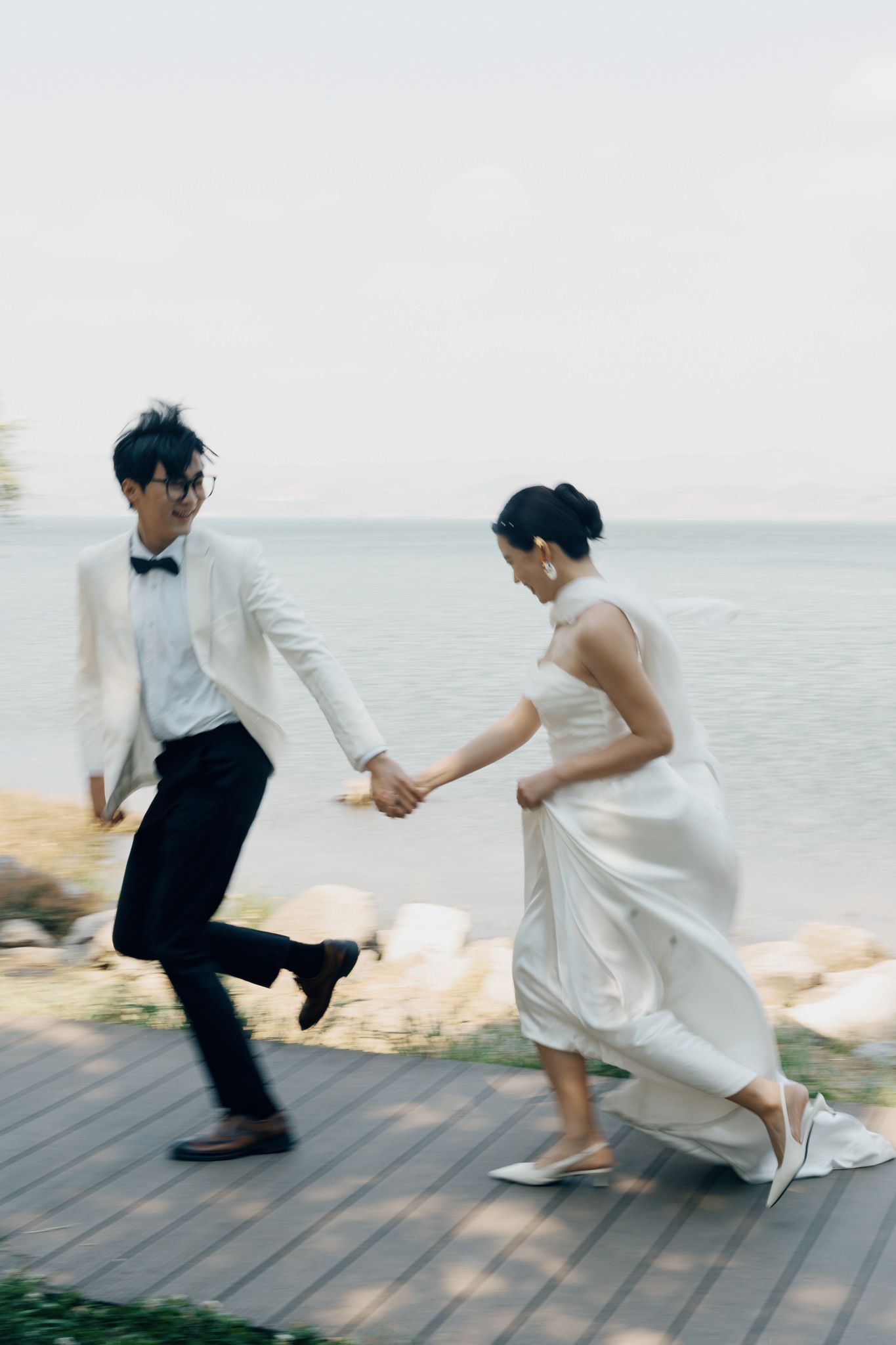 Bride and groom holding hands and running on a waterfront deck during their destination wedding portrait session