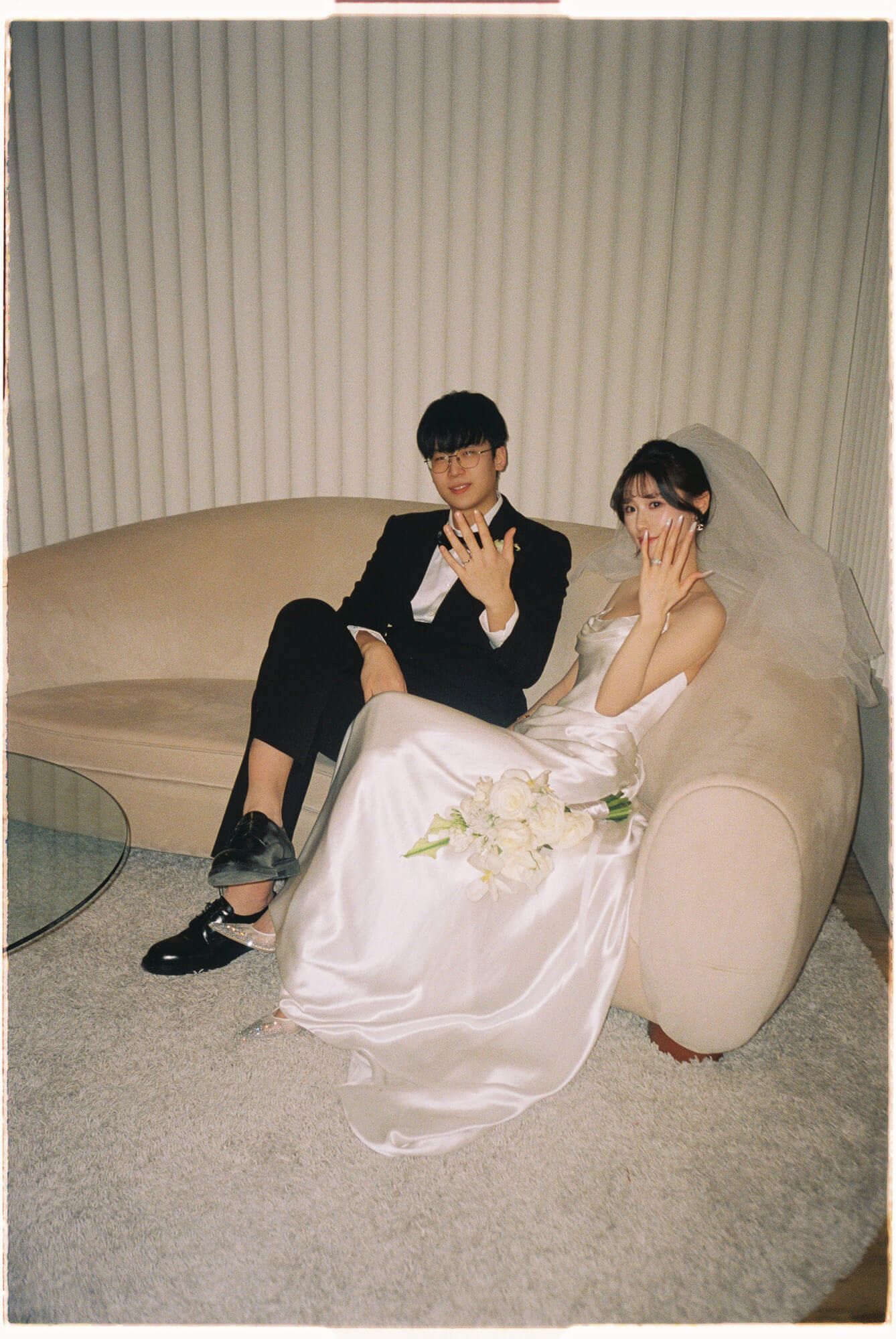 Bride and groom showing their rings on a beige sofa at Archive Studio in Toronto for intimate 35mm film wedding photography.