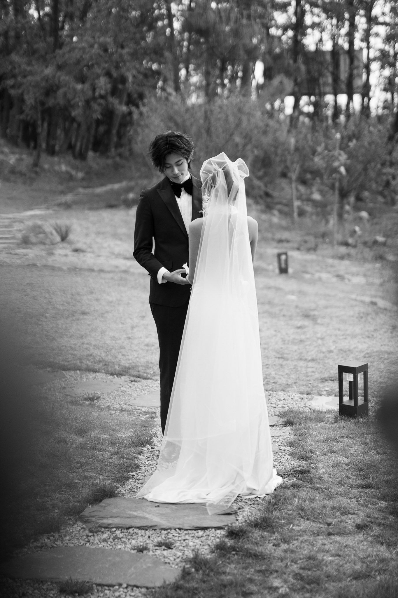 Black and white outdoor portrait of bride in veil and groom in tuxedo among trees during their destination wedding photography session