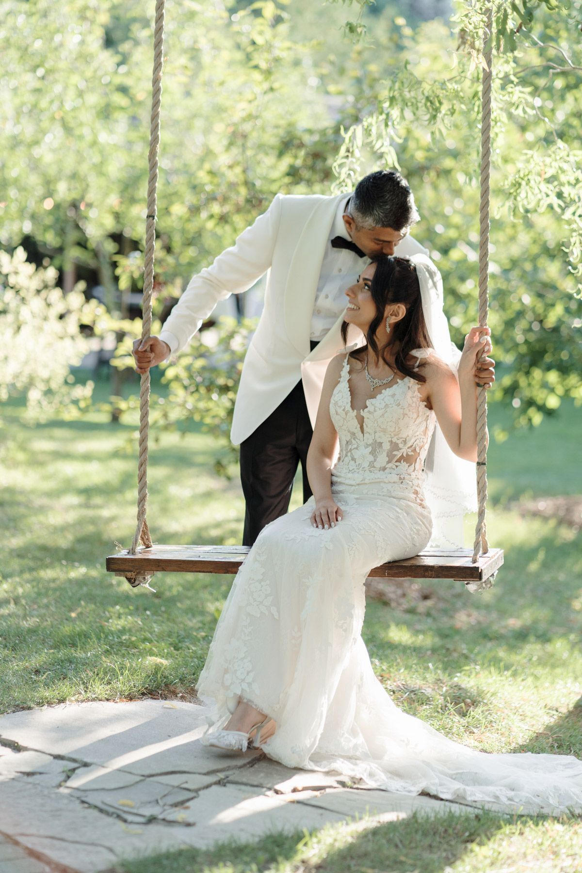 Bride on garden swing as groom leans in for a kiss at Kurtz Orchards in Niagara-on-the-Lake for romantic wedding photography.