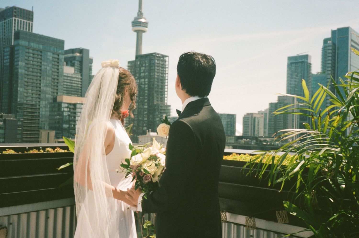 Bride and groom share a romantic moment on a rooftop terrace with Toronto CN Tower skyline in the background.