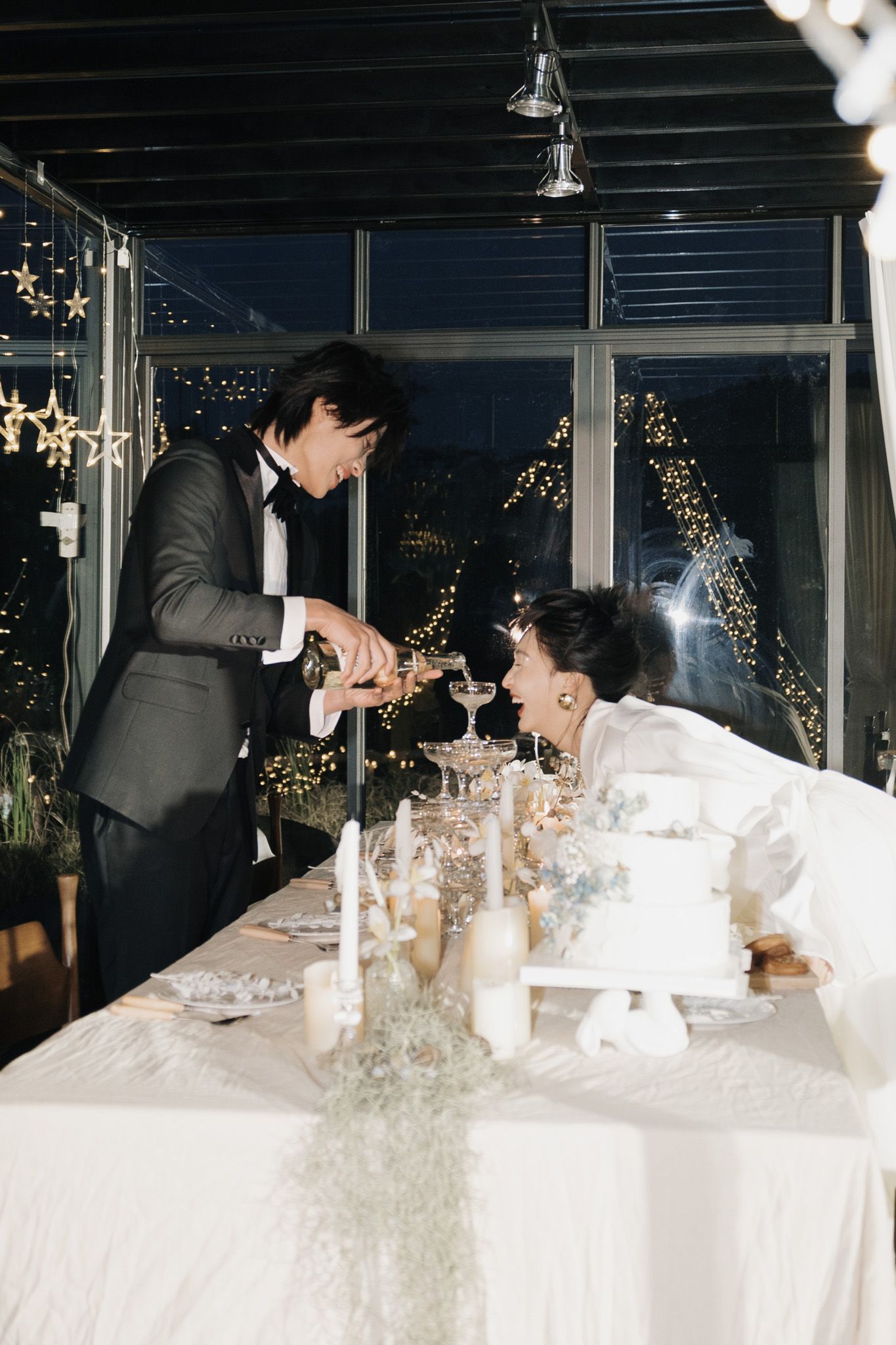 Groom pouring champagne for the bride at a candlelit reception table during their elegant destination wedding celebration.