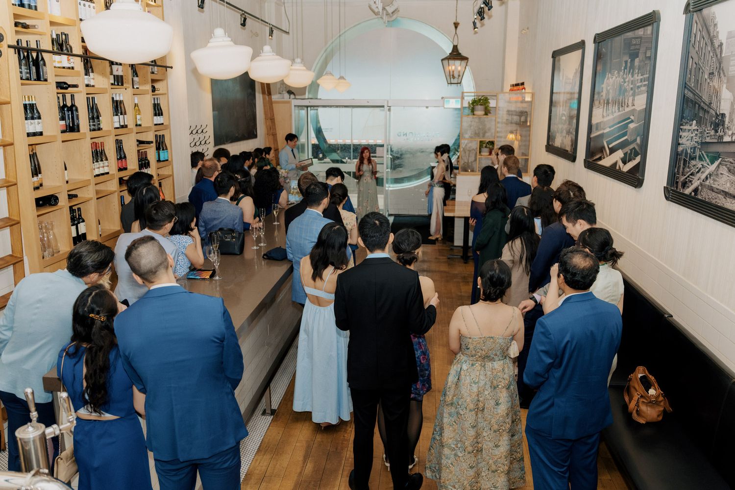 Guests gather indoors for an intimate wedding ceremony in a stylish venue with wooden floors and framed artwork.
