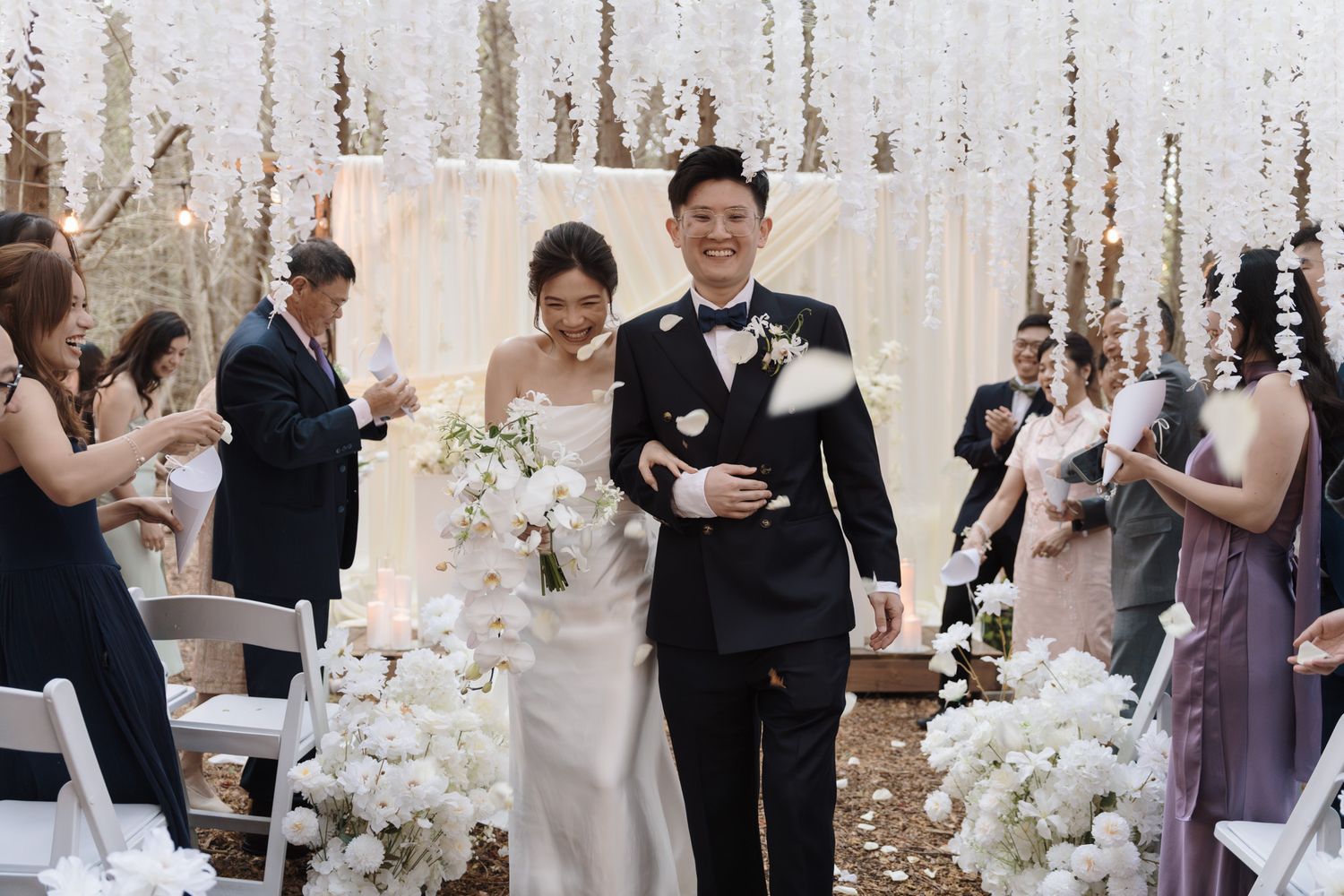 Asian newlyweds walking down the aisle as guests toss petals at a Razi Estate forest wedding ceremony in Toronto. Schomberg, ON