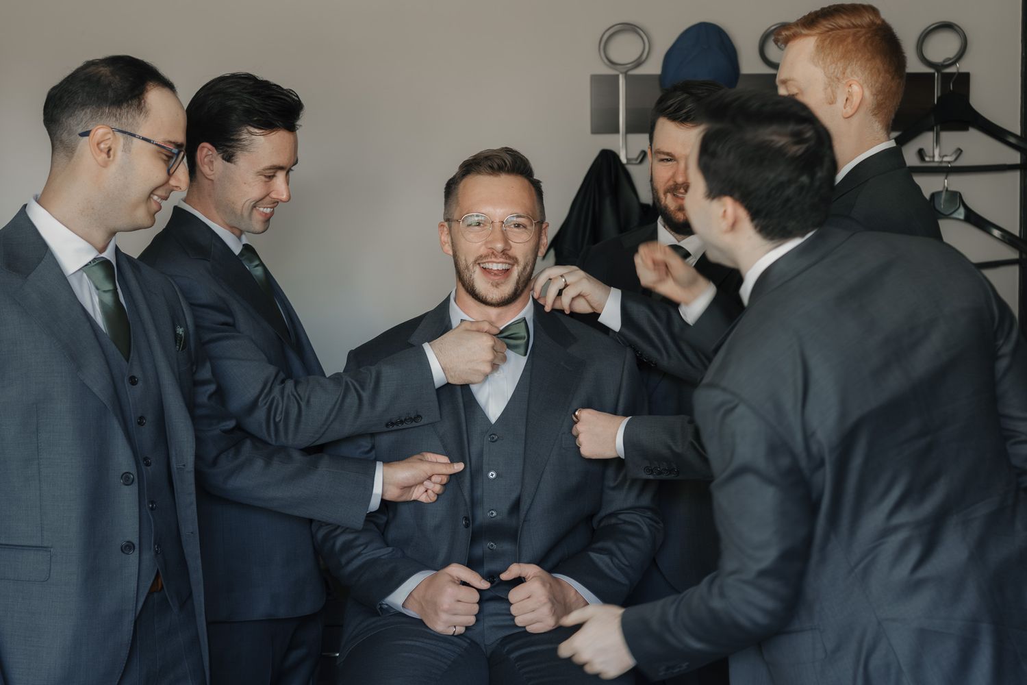Groomsmen helping the groom adjust his suit at The Manor in King City before the wedding ceremony.