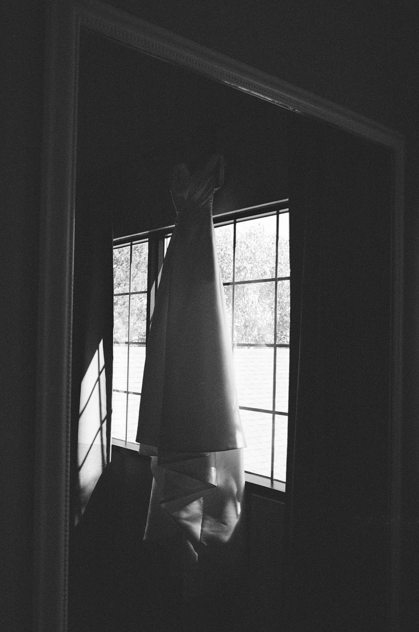 Black and white wedding dress hanging in a doorway with natural window light at The Manor in King City wedding morning.