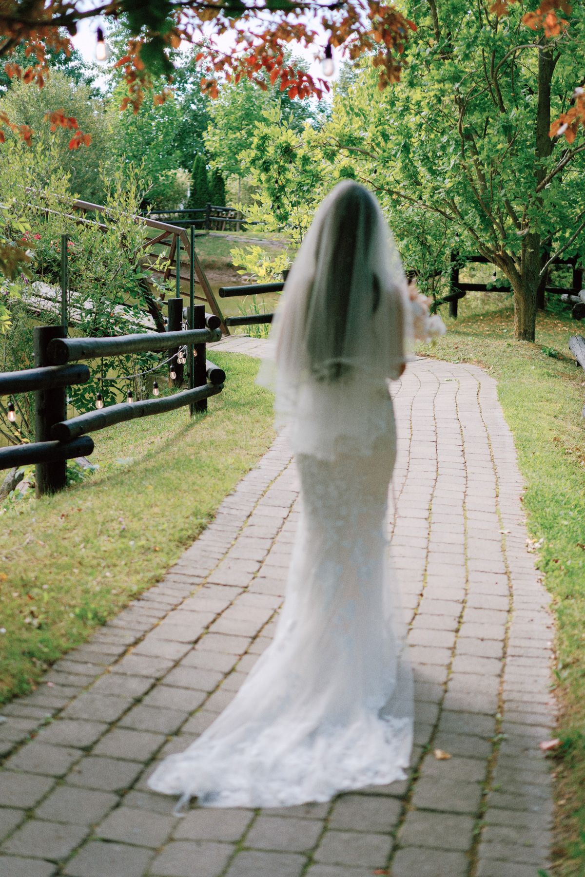 Bride in lace gown and veil walking a brick garden path at Kurtz Orchards in Niagara-on-the-Lake for romantic wedding photography.