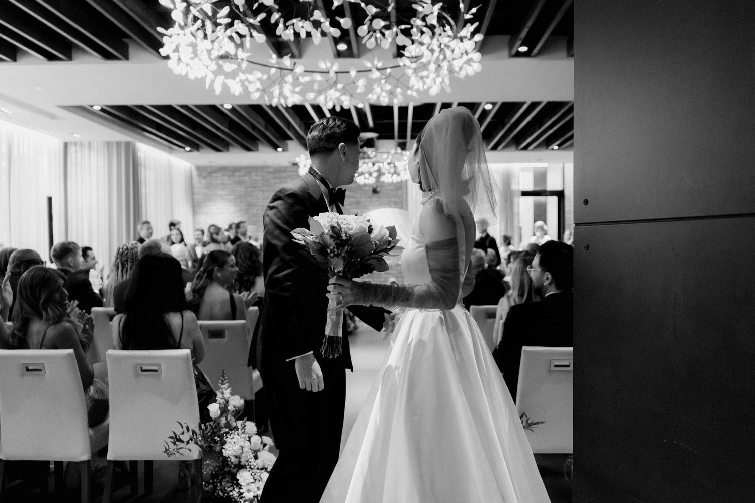 Bride and groom sharing a kiss beneath a floral chandelier during their ceremony at The Village Loft in North York for a Toronto Wedding
