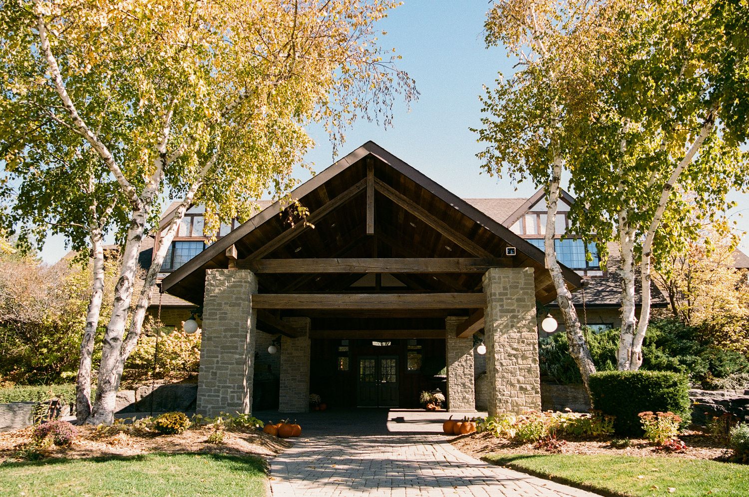 Craftsman-style lodge entrance with stone pillars and autumn birch trees at The Manor in King City wedding venue.