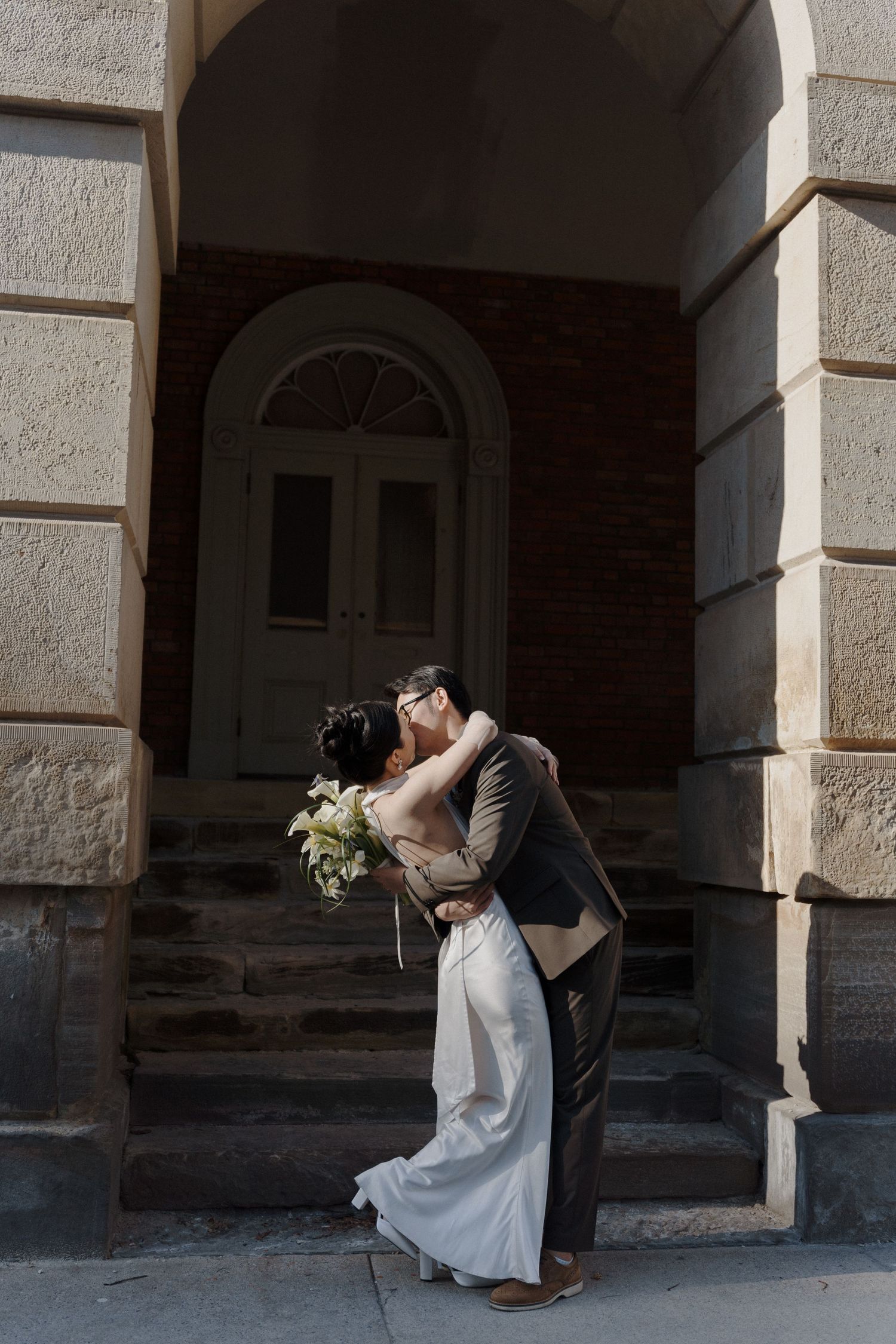 Bride and groom kissing outside Osgoode Hall’s arched brick doorway for timeless Toronto City Hall wedding photography.