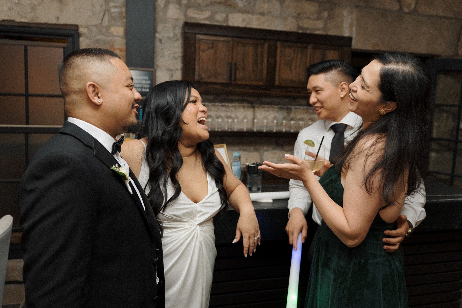 Two couples laughing together at a wedding reception inside Cambridge Mill in Cambridge, Ontario for candid wedding photography.