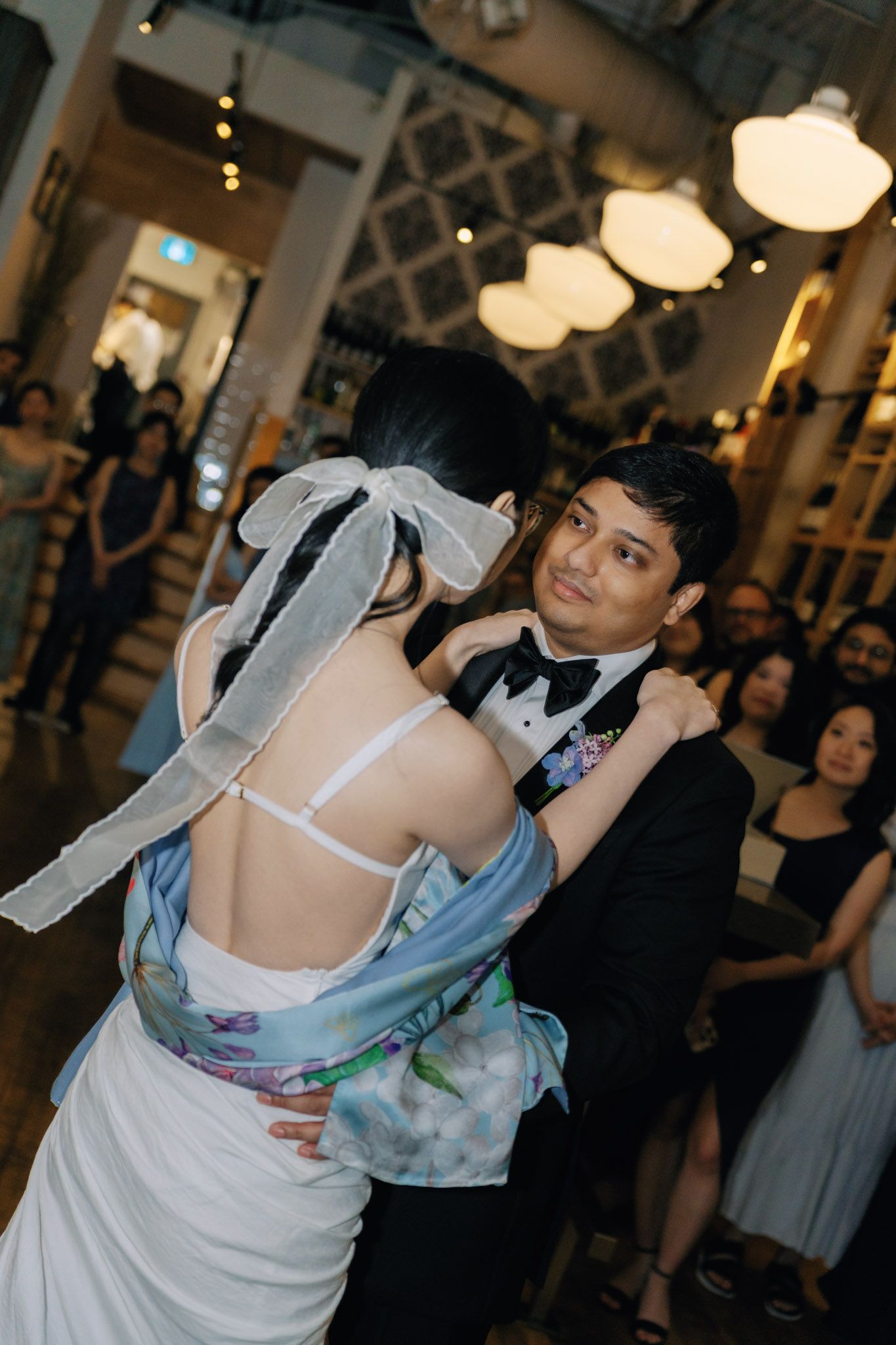Bride and groom share their first dance at an elegant indoor wedding reception, surrounded by guests and warm lighting.