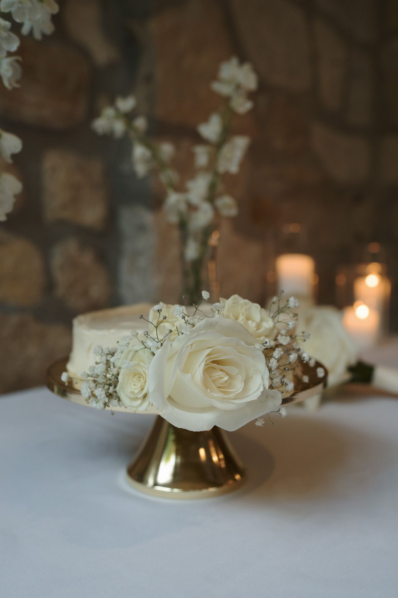 White rose wedding cake on a gold pedestal with candles at Cambridge Mill in Cambridge, Ontario for editorial wedding photography