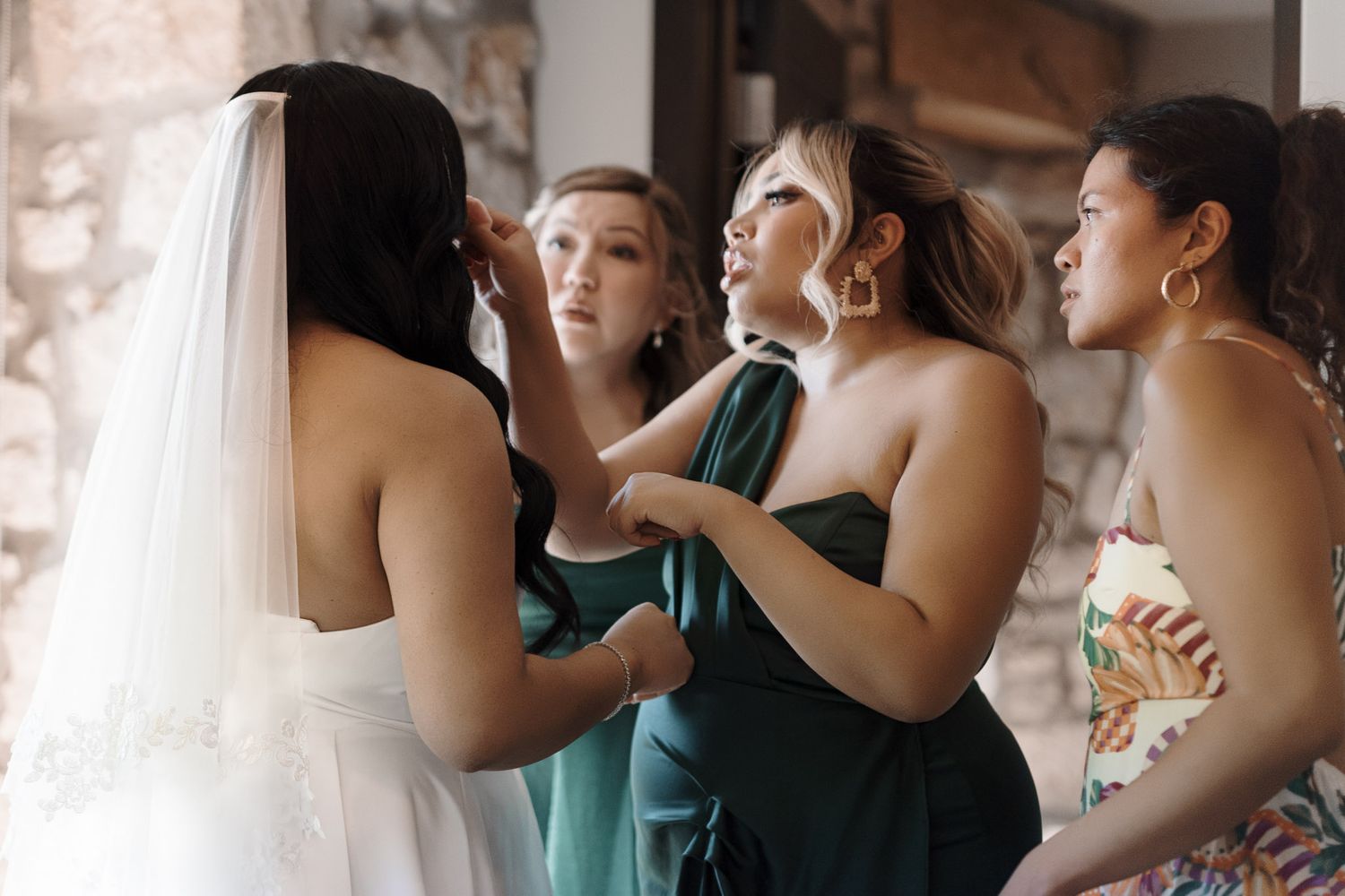 Bridesmaids in green dresses help a bride with her veil before the wedding ceremony.