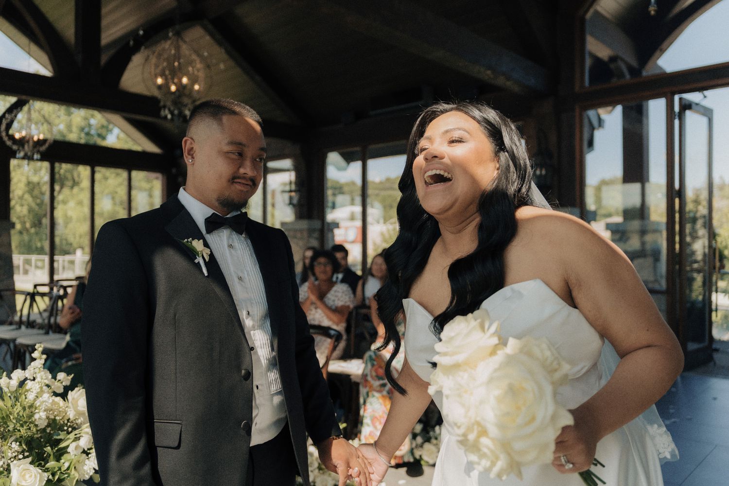 Bride laughing with groom during their ceremony at Cambridge Mill in Cambridge, Ontario for candid wedding photography.