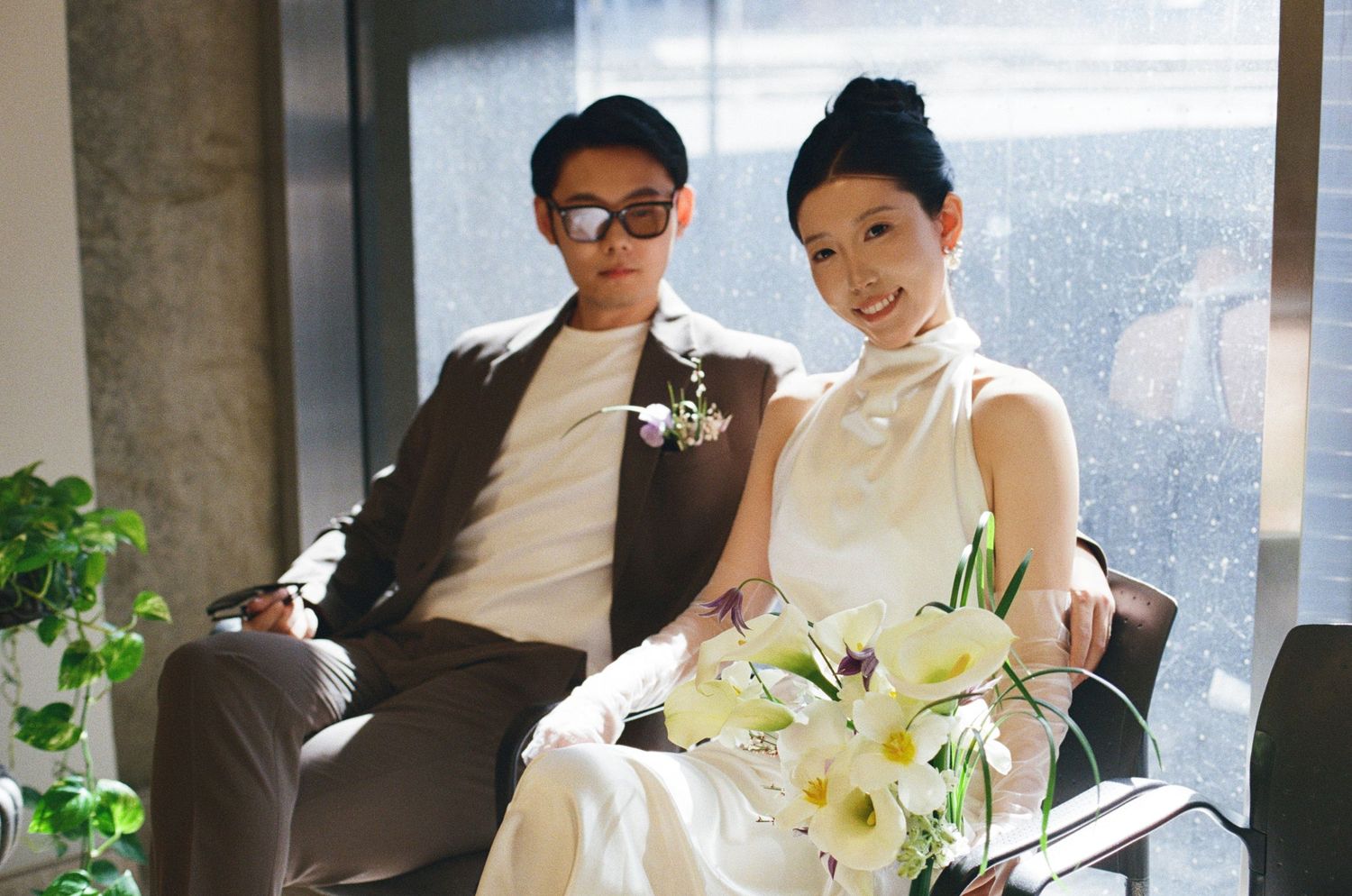 Bride and groom eloping at Toronto City Hall, seated together with sunglasses, white dress, and flowers for candid wedding photography. 35mm