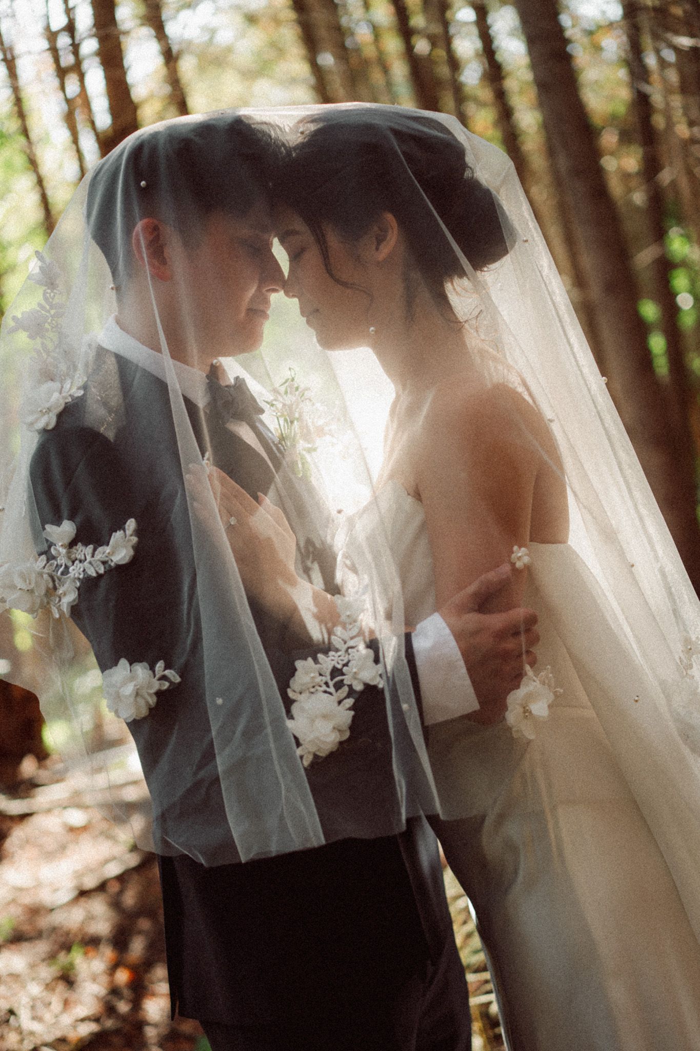 Bride and groom sharing an intimate moment beneath a lace veil in the sunlit forest at Razi Estate in Schomberg for cinematic wedding photo