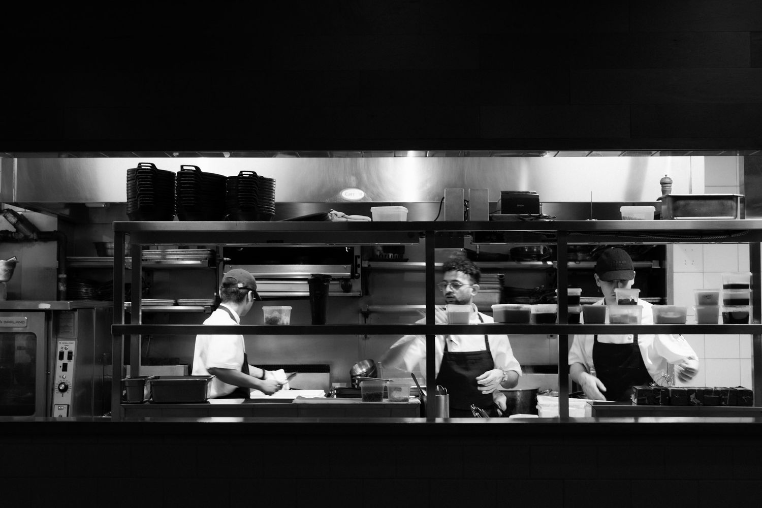 Black and white photo of chefs working in a professional restaurant kitchen with metal shelving and equipment.