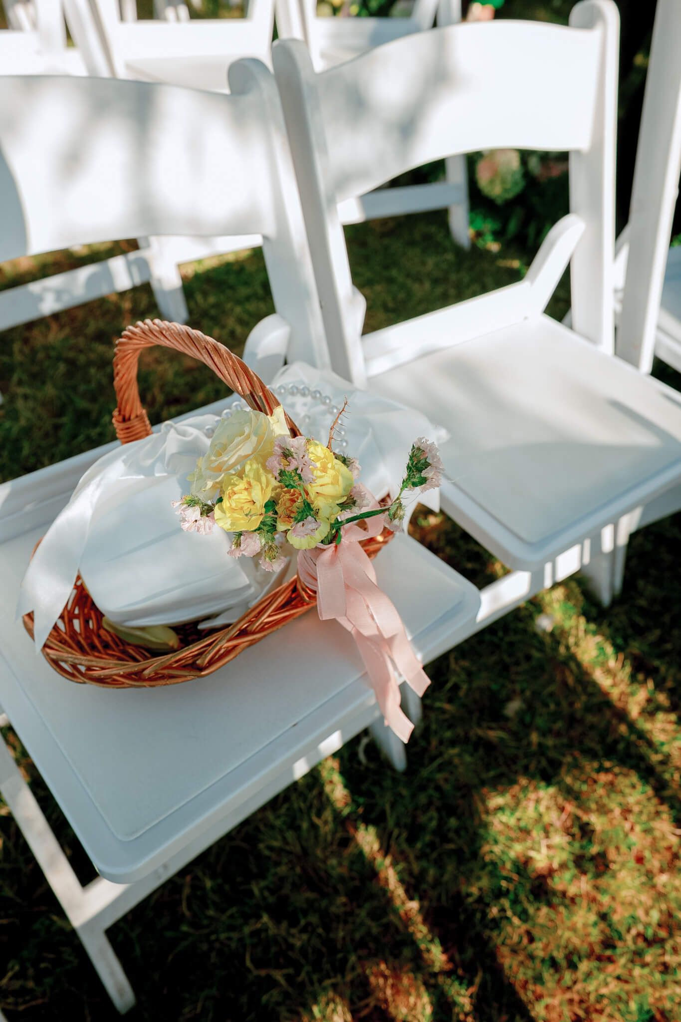 Wicker basket with yellow roses and pink ribbon on white garden chair at Kurtz Orchards in Niagara-on-the-Lake wedding ceremony.