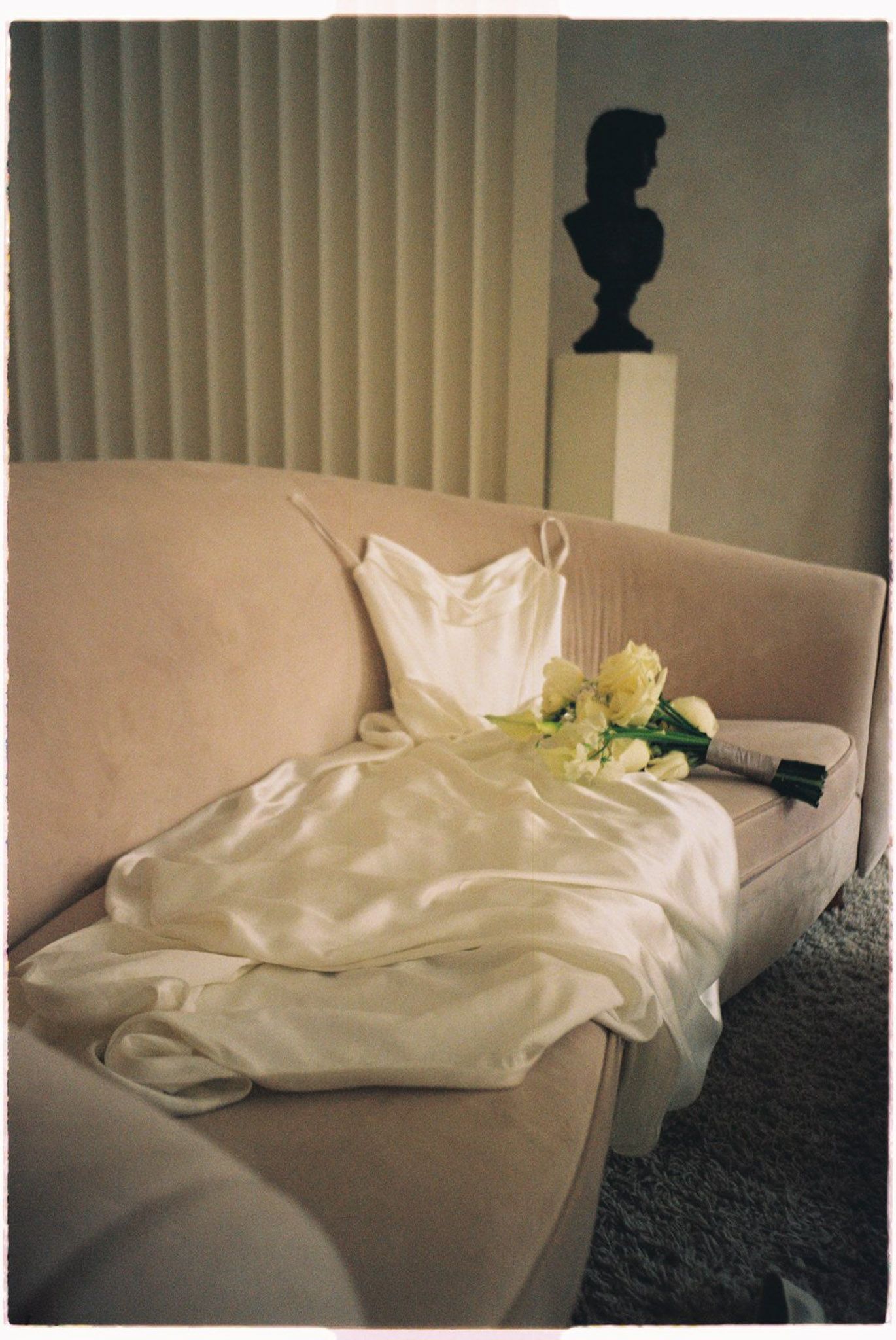 White satin wedding dress and yellow rose bouquet on a blush velvet sofa at Archive Studio in Toronto for editorial wedding photography