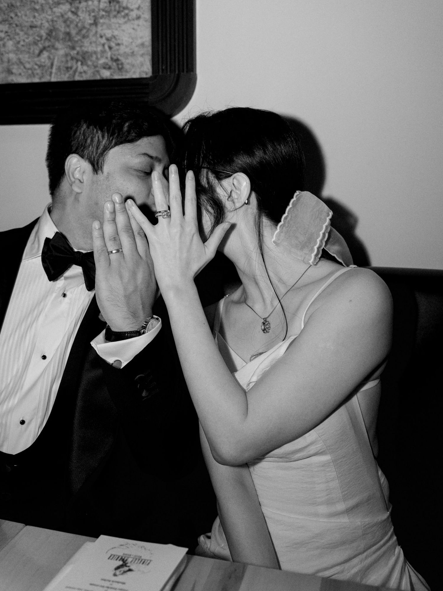Black and white photo of a couple in wedding attire sharing a kiss, bride in white dress, groom in tuxedo.
