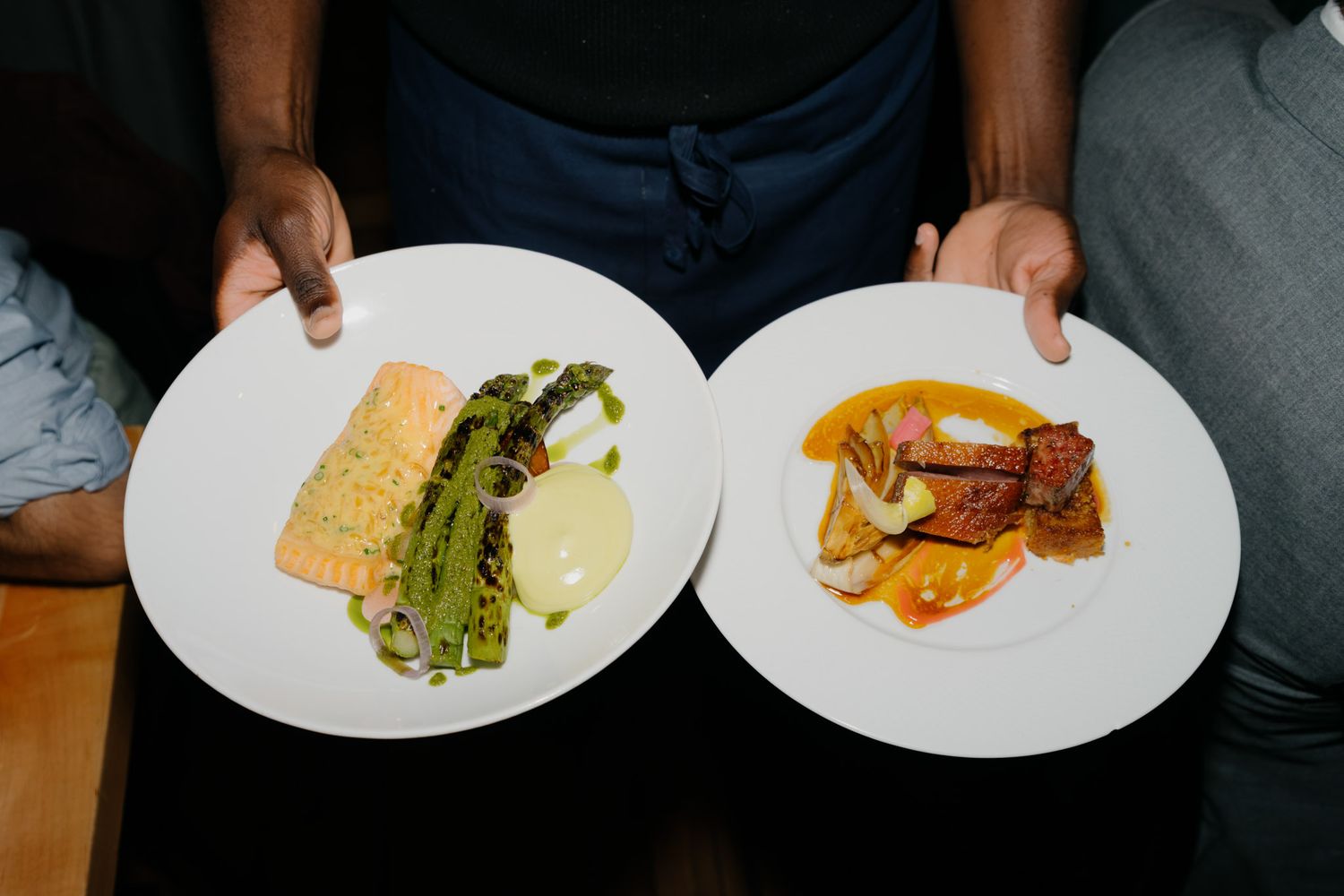Two elegant restaurant plates with gourmet dishes including salmon with greens and seared meat with vegetables held by a waiter.