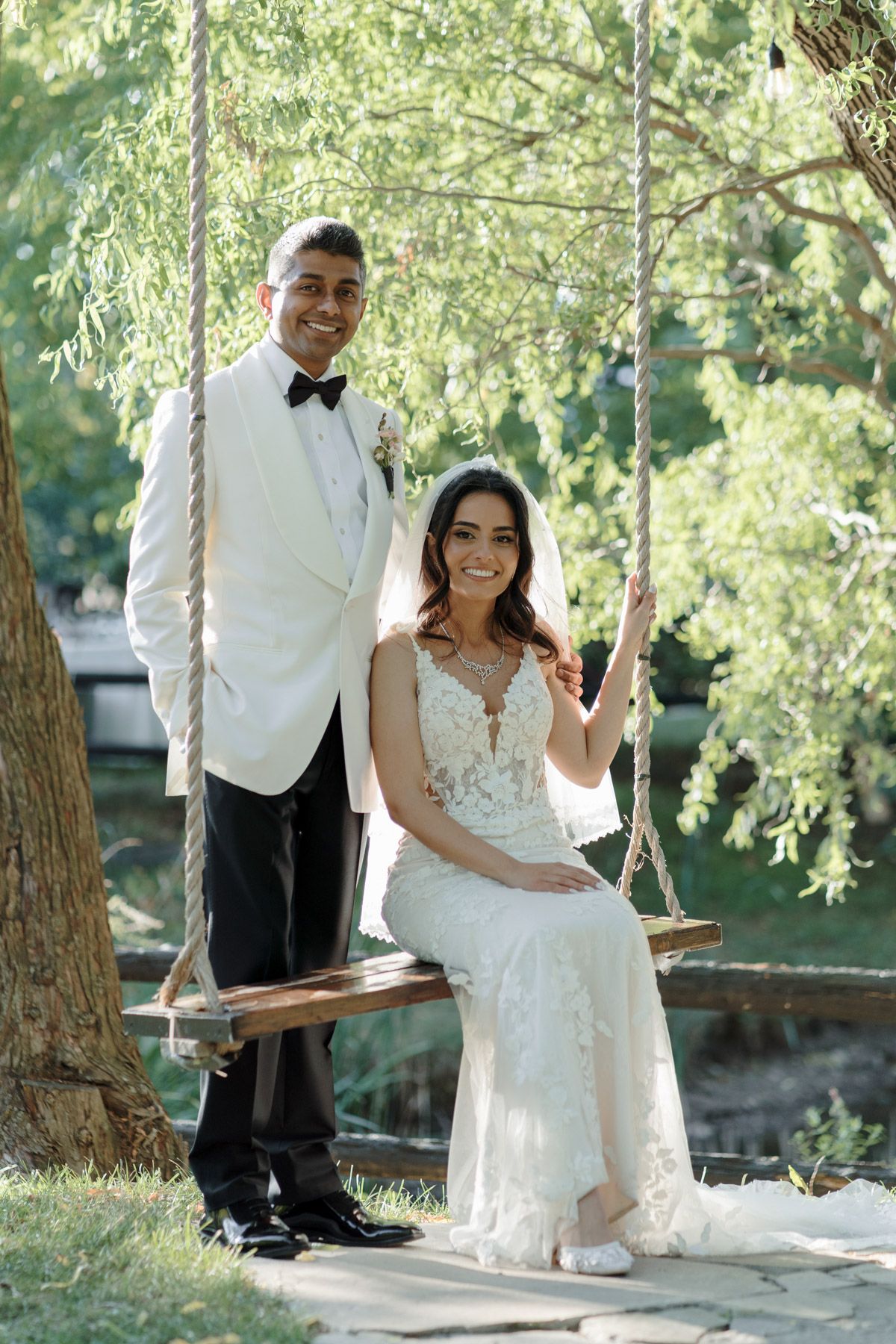Bride on a wooden swing with groom beside her at Kurtz Orchards in Niagara-on-the-Lake for romantic wedding portraits.