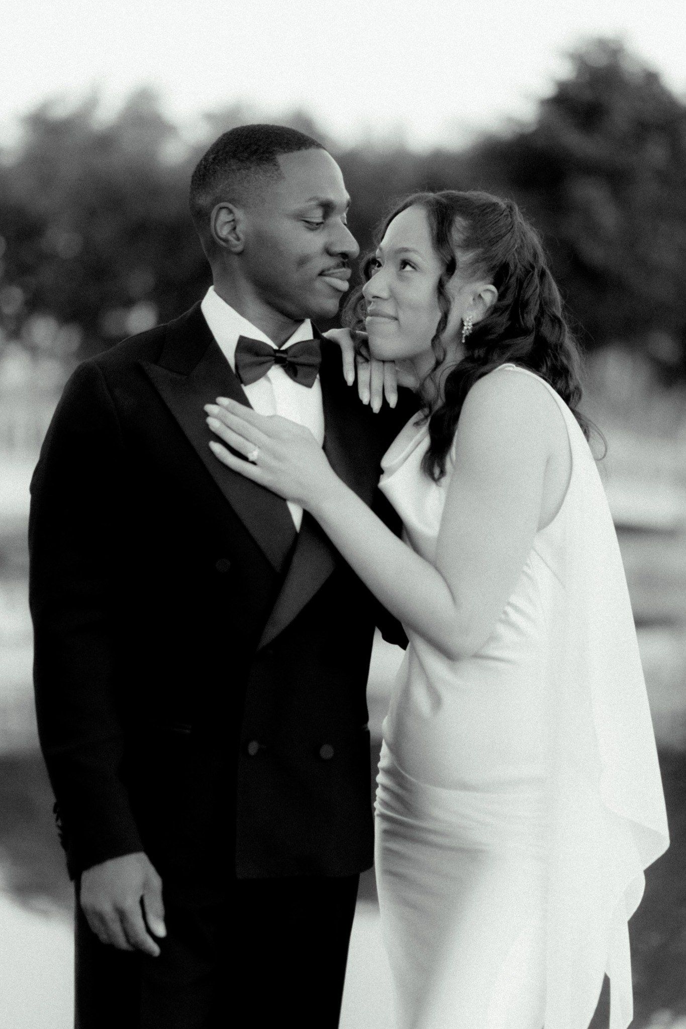 Black and white photo of a couple in wedding attire, bride in white dress embracing groom in tuxedo outdoors.