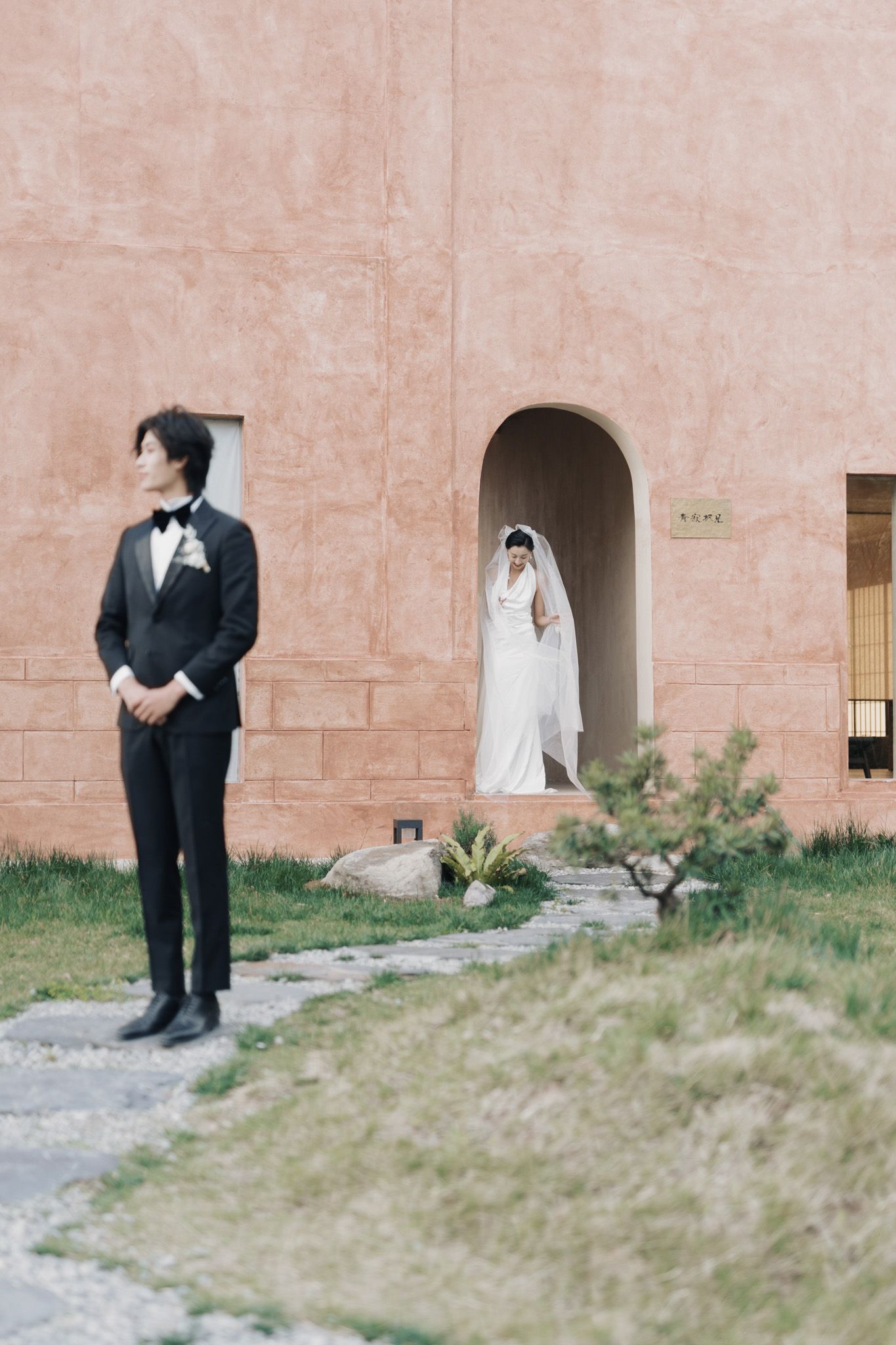 Bride emerging from an arched doorway as groom waits outside during their destination wedding editorial portraits