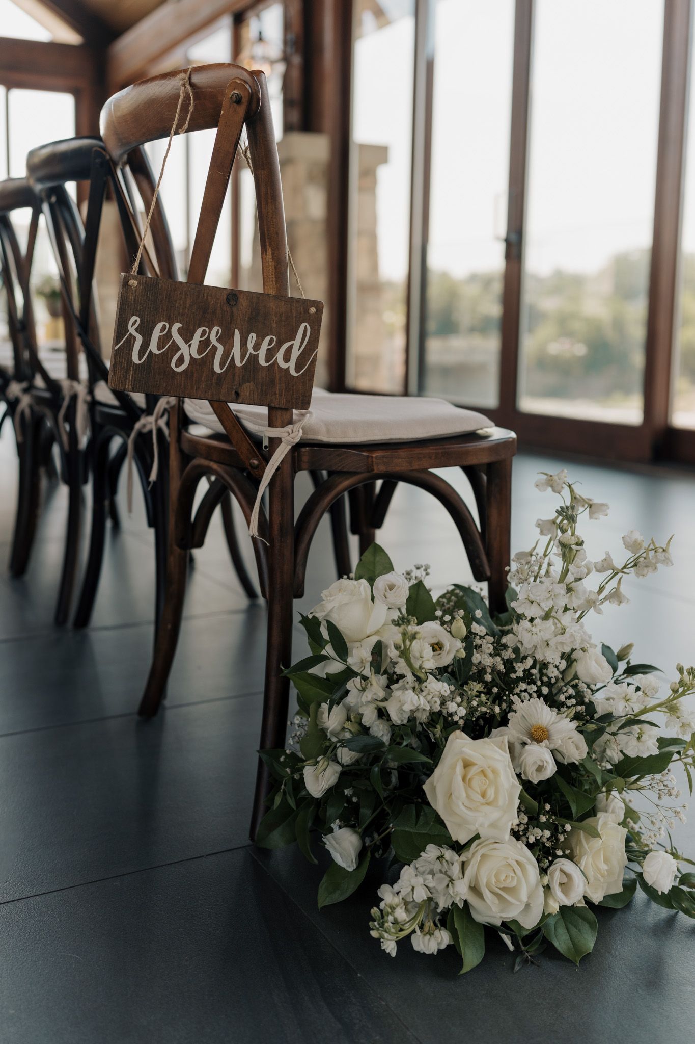 Reserved cross-back chair with white rose florals at Cambridge Mill in Cambridge, Ontario for elegant wedding ceremony photography.