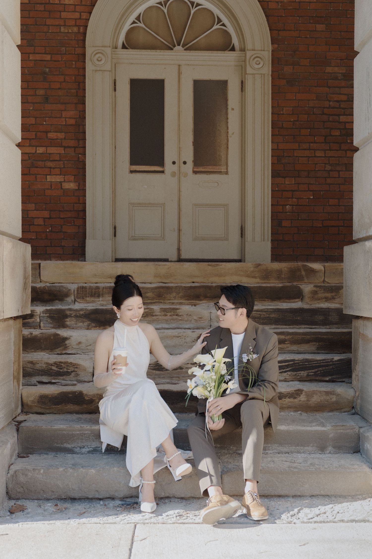 Newlyweds sitting on Osgoode Hall steps with coffee and white flowers for quiet Toronto City Hall wedding photography.