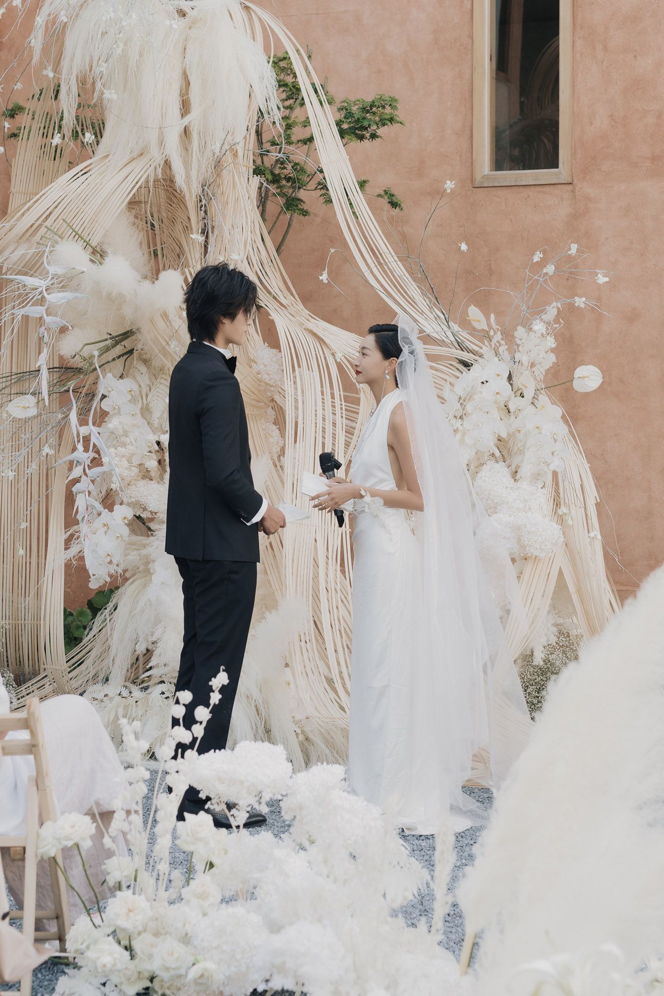 Bride and groom exchanging vows at an elegant outdoor destination wedding ceremony with white florals and macramé décor