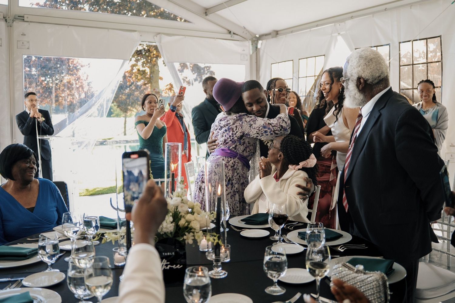 Guests celebrating and hugging at an elegant wedding reception under a white tent with decorated tables.
