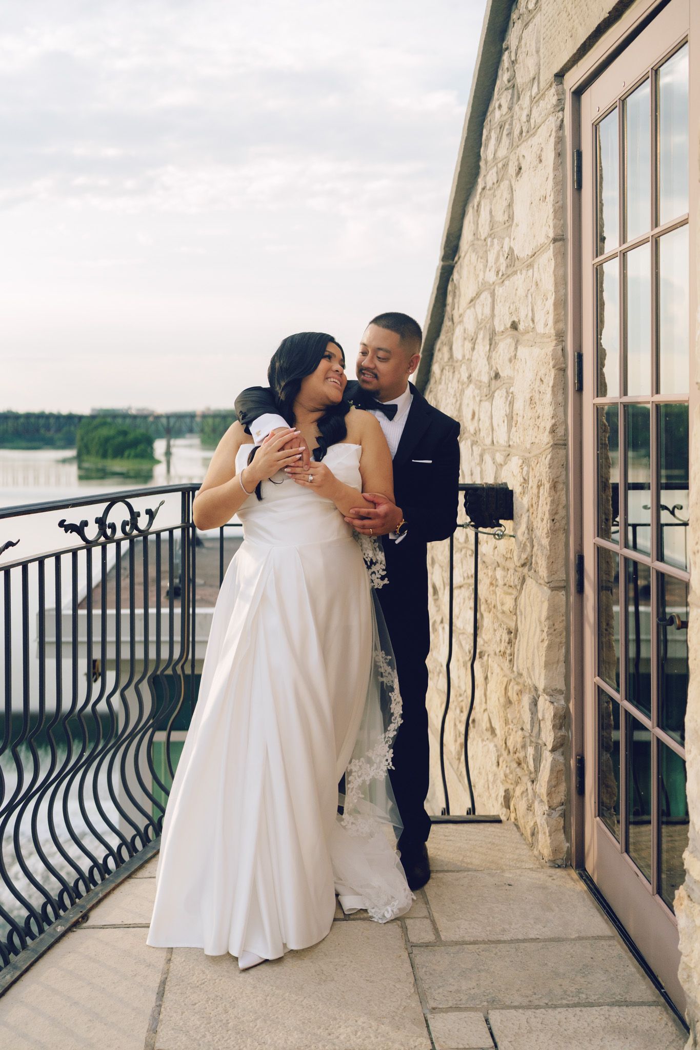 Bride and groom embracing on a stone balcony at Cambridge Mill in Cambridge, Ontario with scenic waterfront wedding views.