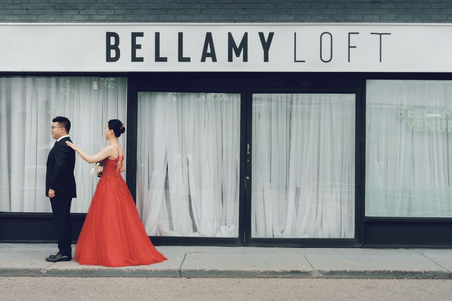 Couple in formal wear posing outside Bellamy Loft in North York, Toronto as bride adjusts groom’s suit jacket.