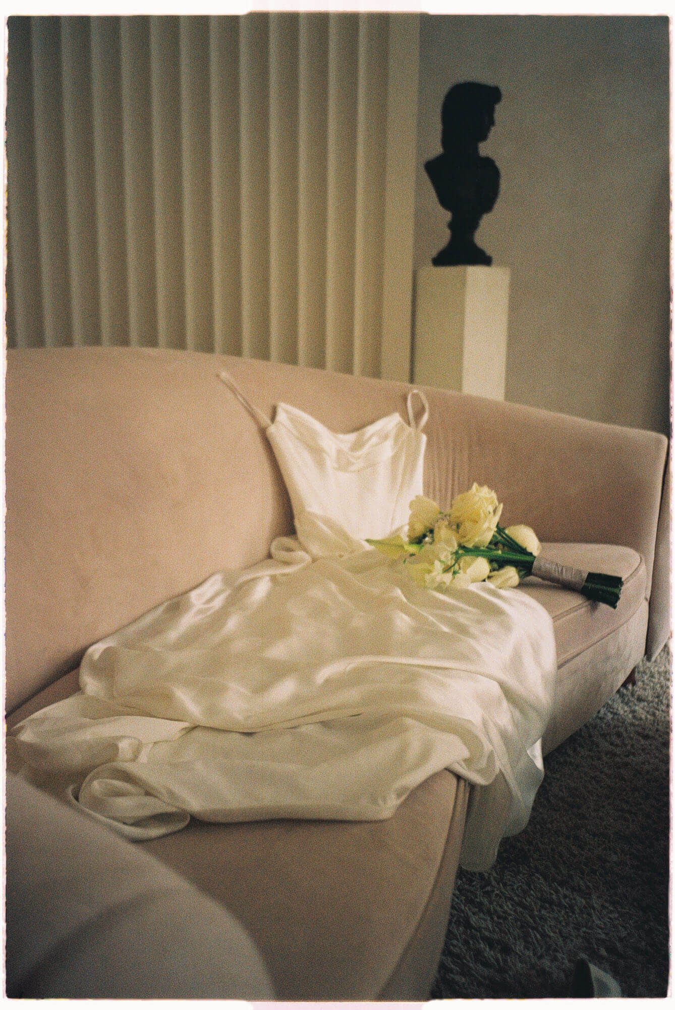 White satin wedding dress with yellow rose bouquet on blush velvet sofa at Archive Studio in Toronto for intimate wedding photography. 35mm