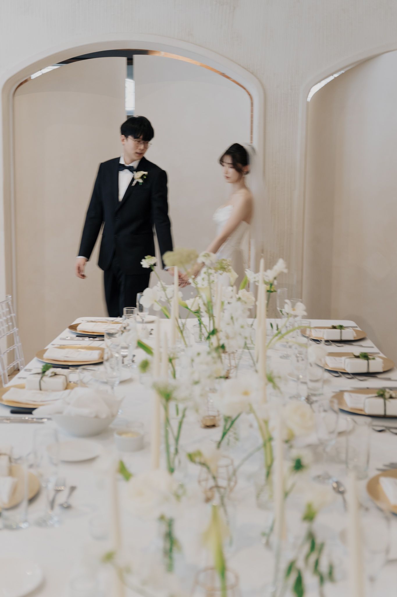 Elegant wedding reception table with white florals as bride and groom enter through an arched doorway at Archive Studio, Toronto