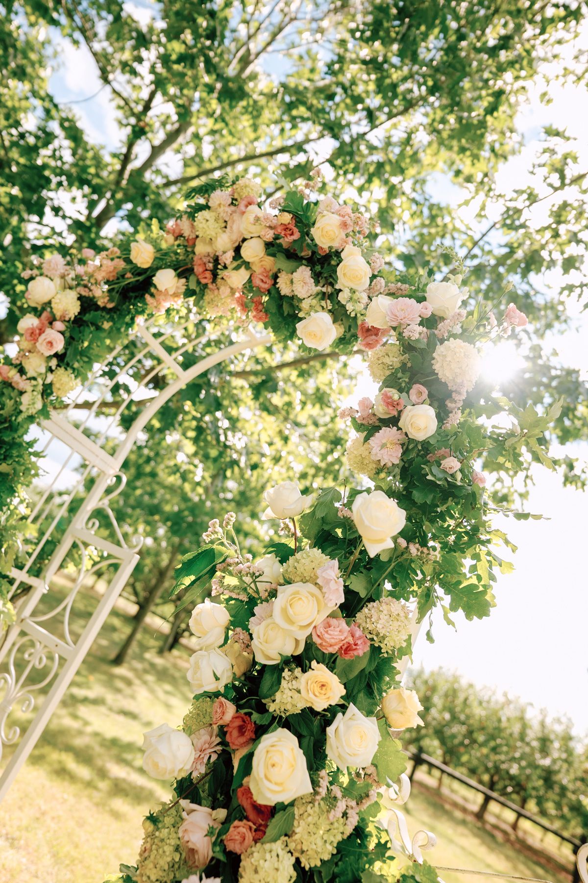 White rose floral wedding arch with greenery in a sunlit garden at Kurtz Orchards in Niagara-on-the-Lake outdoor ceremony.