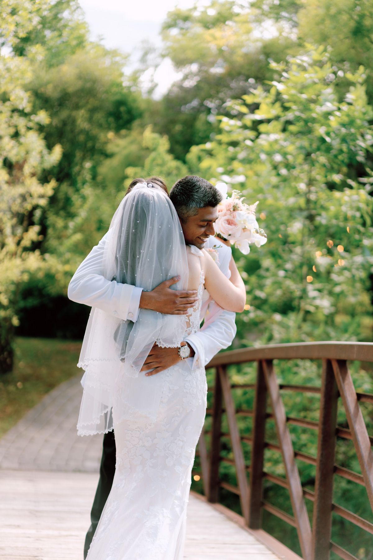 Bride and groom embracing on a garden bridge with pink bouquet at Kurtz Orchards in Niagara-on-the-Lake for romantic wedding photography.