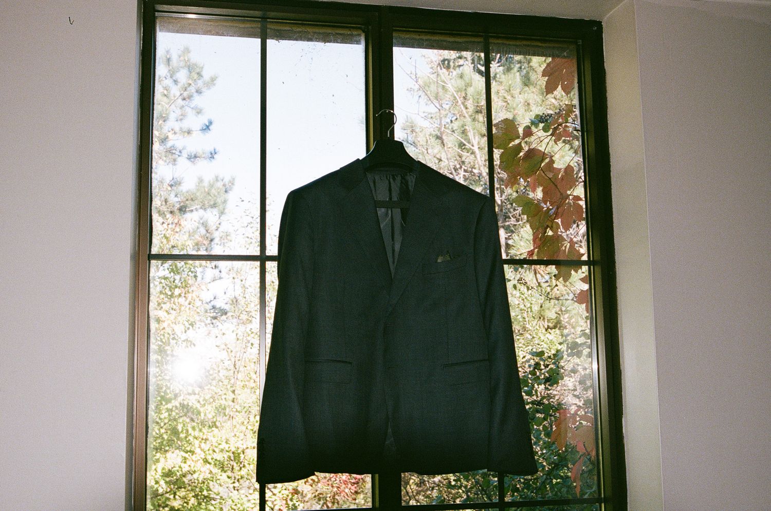 Groom’s dark suit jacket hanging by a window with autumn foliage at The Manor in King City wedding morning.