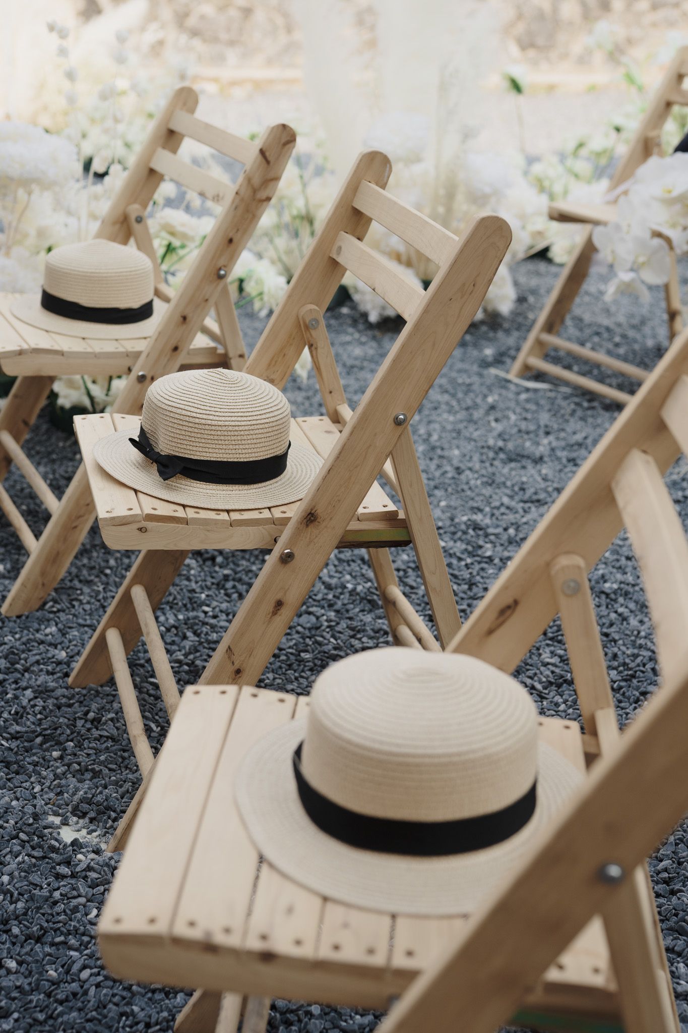 Wooden ceremony chairs with straw boater hats on gravel for an outdoor Toronto wedding ceremony and documentary wedding photography