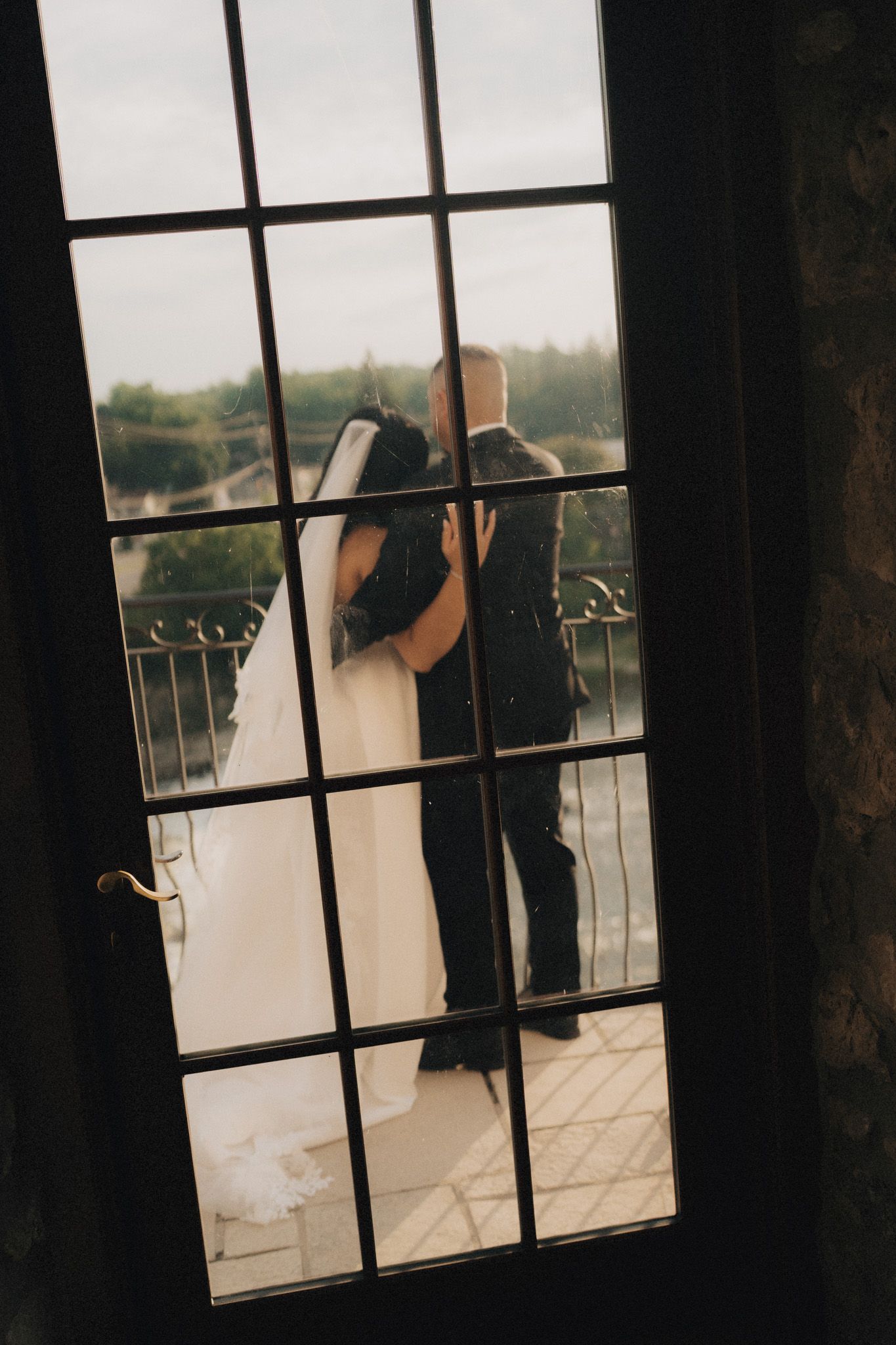 Bride and groom kissing on a balcony through French doors at Cambridge Mill in Cambridge for romantic wedding photography.