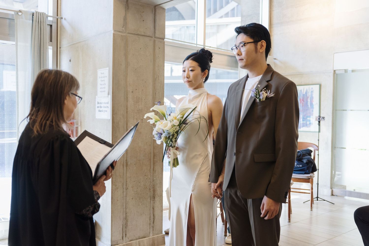 Couple exchanging vows before an officiant during a candid Toronto City Hall civil wedding ceremony with bridal bouquet.