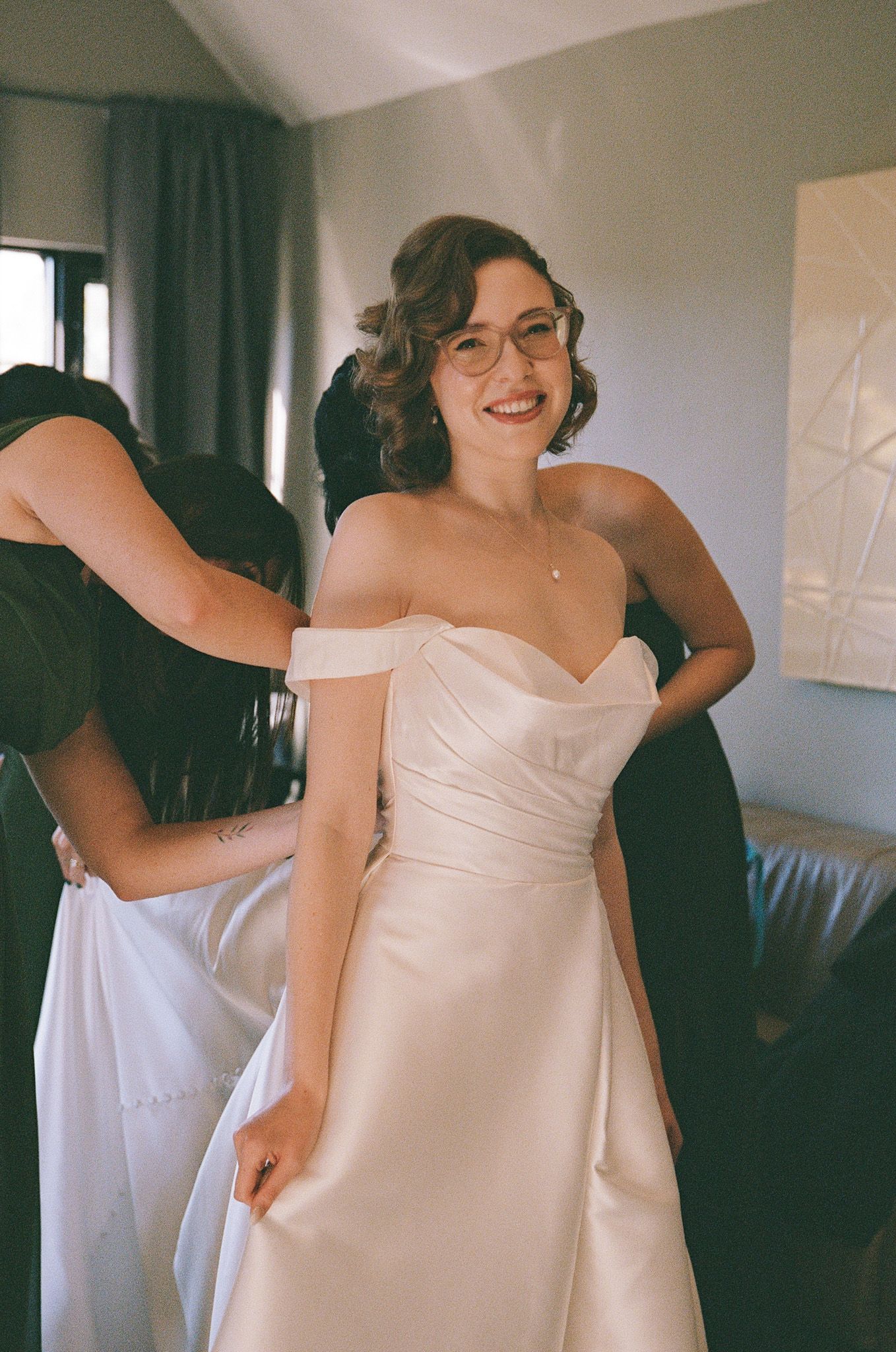Bride in glasses getting help into her wedding gown by bridesmaids at The Manor in King City wedding morning.