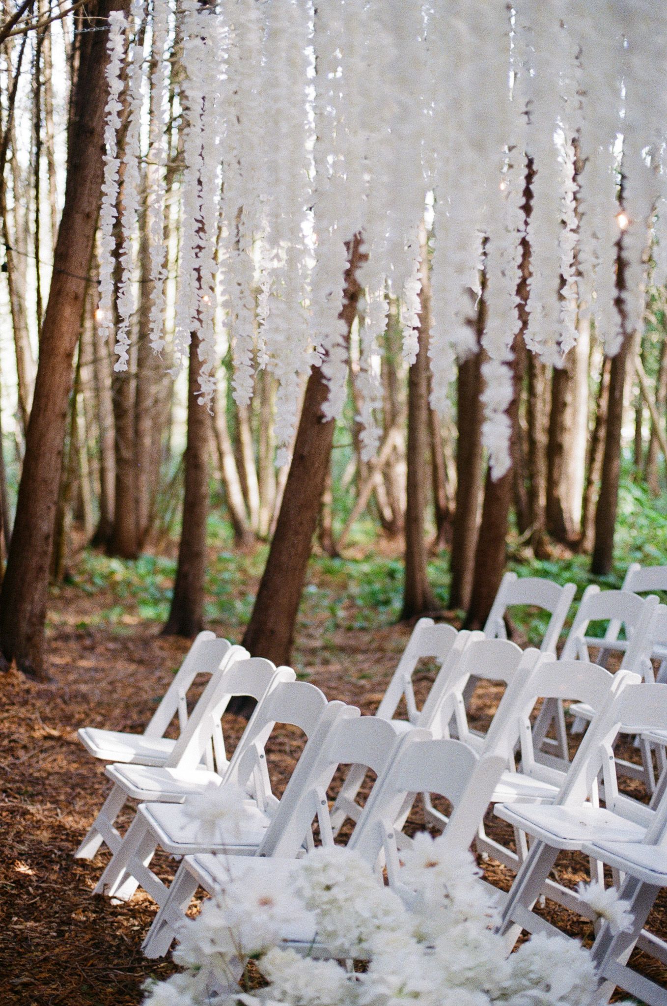 White folding chairs beneath hanging floral garlands among tall trees at Razi Estate in Schomberg for forest wedding photography.
