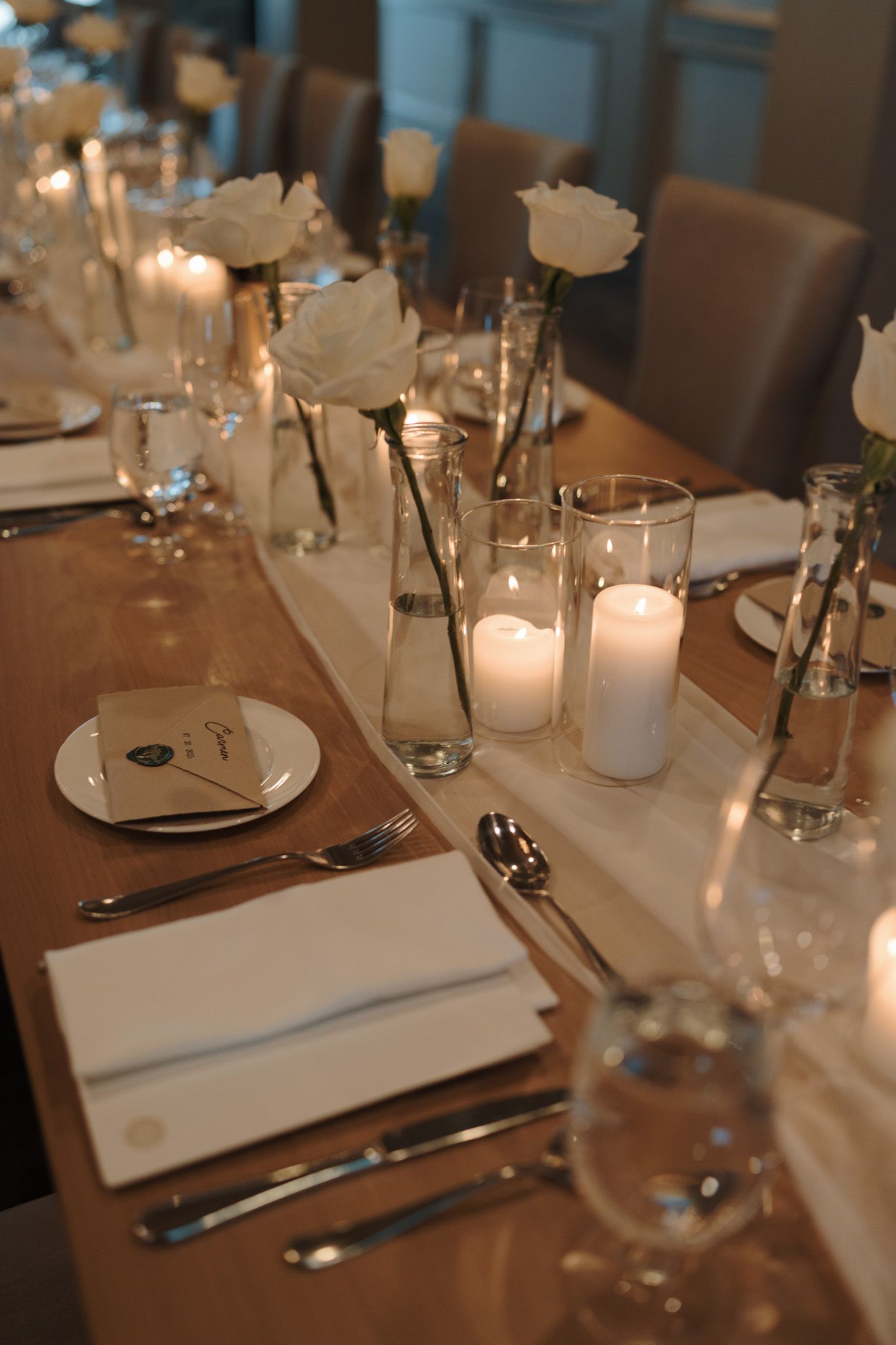 Wedding table décor with white roses, pillar candles, and place settings at Cambridge Mill in Cambridge, Ontario wedding reception